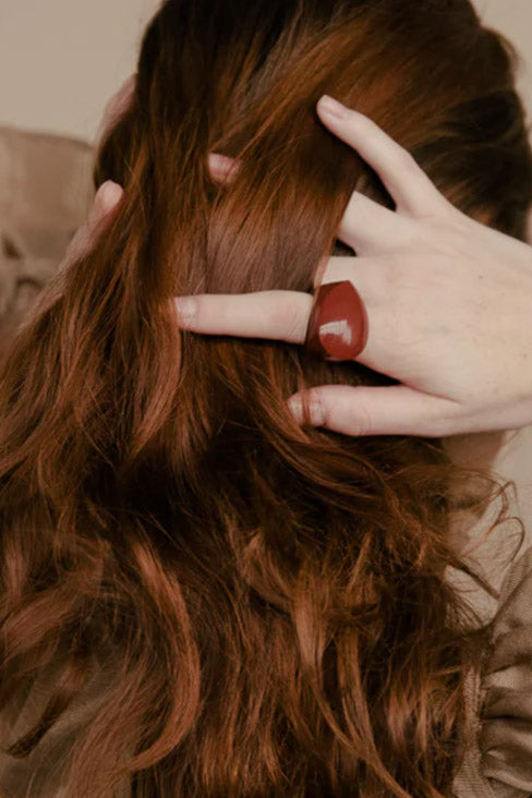 The back of a head of long luxurious deep red hair with finges running through it - one finger has a deep red baubble ring  by Kathleen Whitaker