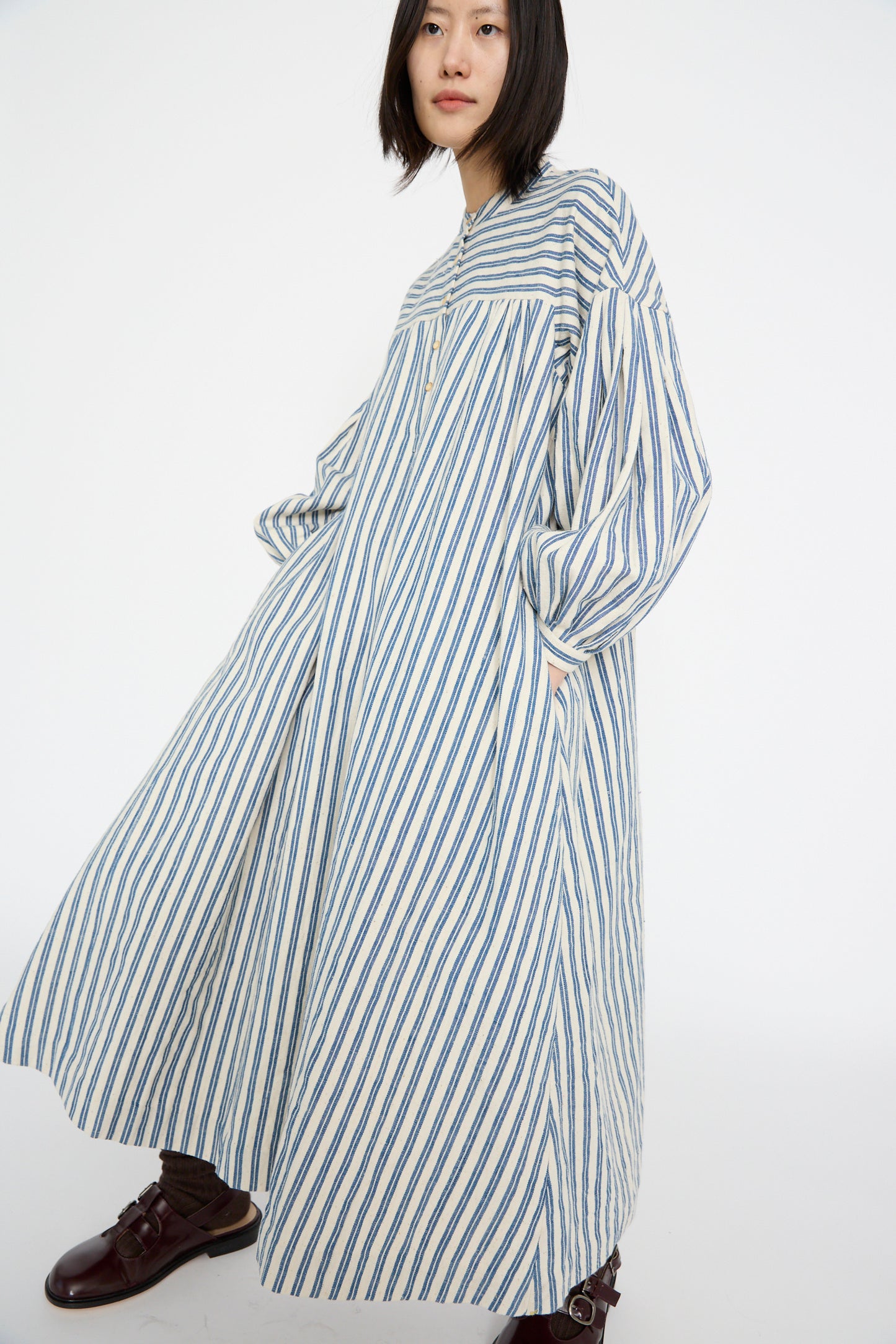 Someone is wearing the 11.11 Cotton Gurue Dress in Medium Indigo Stripe, made from handwoven cotton, and has one hand in their pocket.