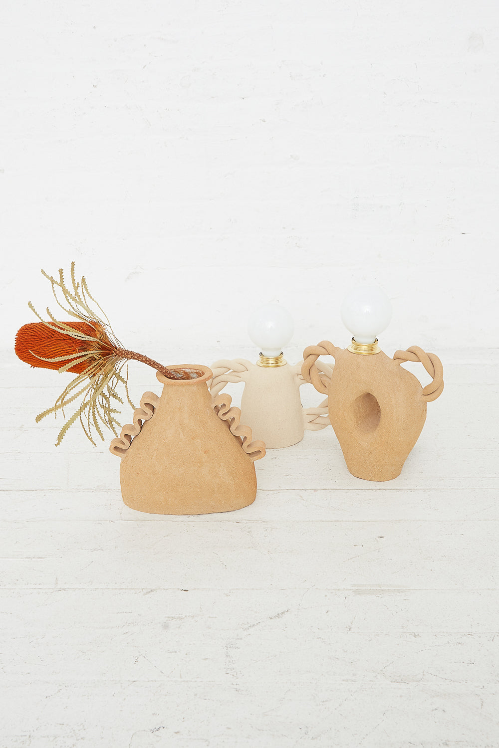 Three decorative Amphora Soleil vases with spherical accents and handles, one holding dried flowers, on a white background. The vases are from Clandestine.
