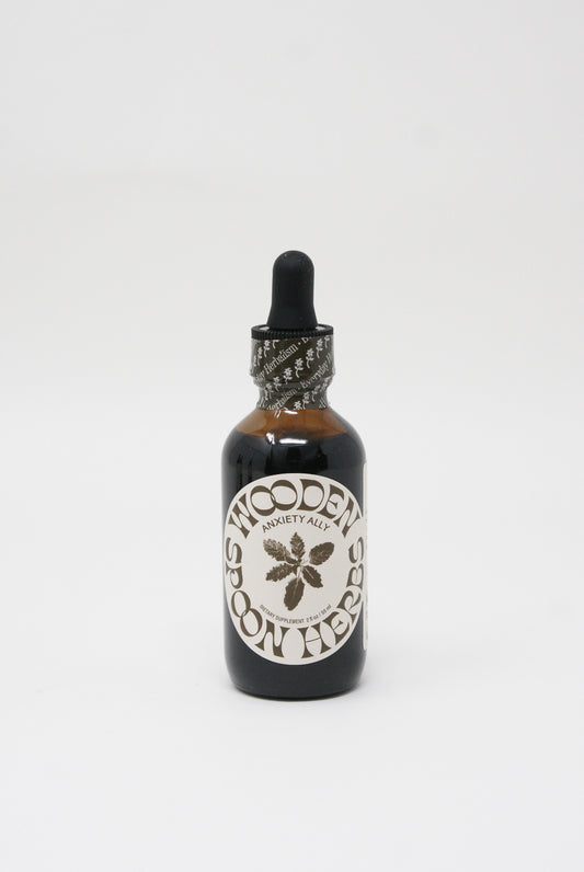 Amber glass dropper bottle labeled "Anxiety Ally Tincture" for herbal use, containing USDA Organic extract to calm nerves, against a white background. Brand name: Wooden Spoon Herbs.