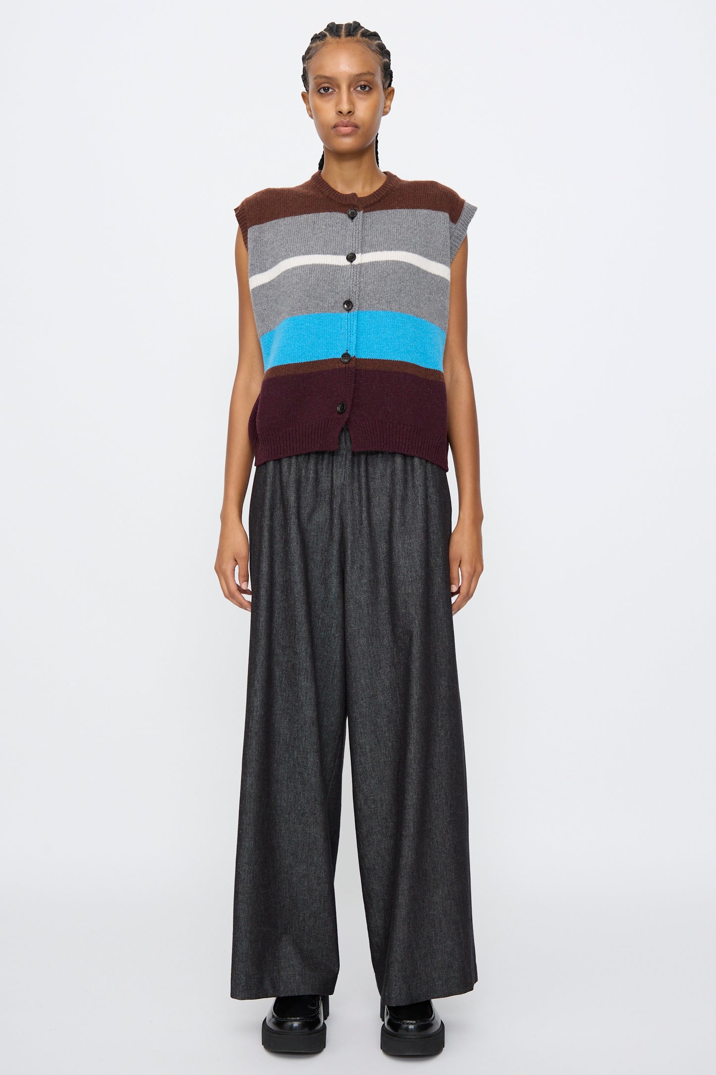 A person stands facing forward, wearing the AVN Funky Vest in Multicolor, a sleeveless Italian wool blend with stripes, paired with wide-leg dark trousers and black shoes against a plain white background.