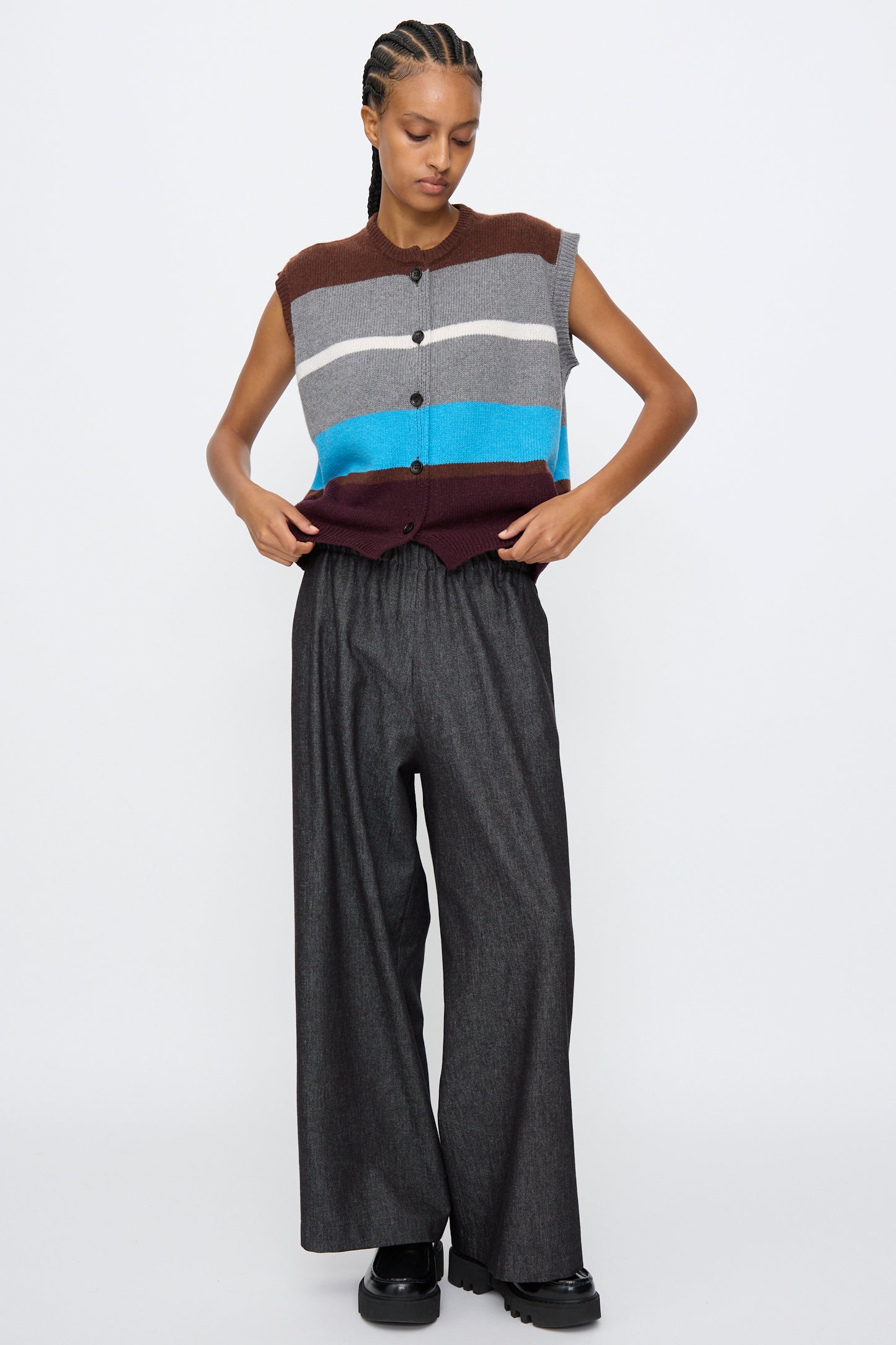 A person wears the AVN Funky Vest in Multicolor, a sleeveless wool blend with stripes, paired with wide-leg dark gray pants, standing against a plain white background.