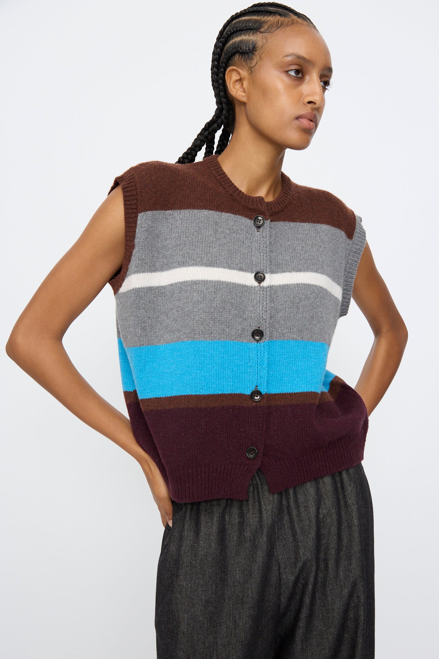 A person wears the AVN Funky Vest in Multicolor—a sleeveless, button-up wool blend vest with brown, grey, white, blue, and burgundy stripes—paired with dark pants.