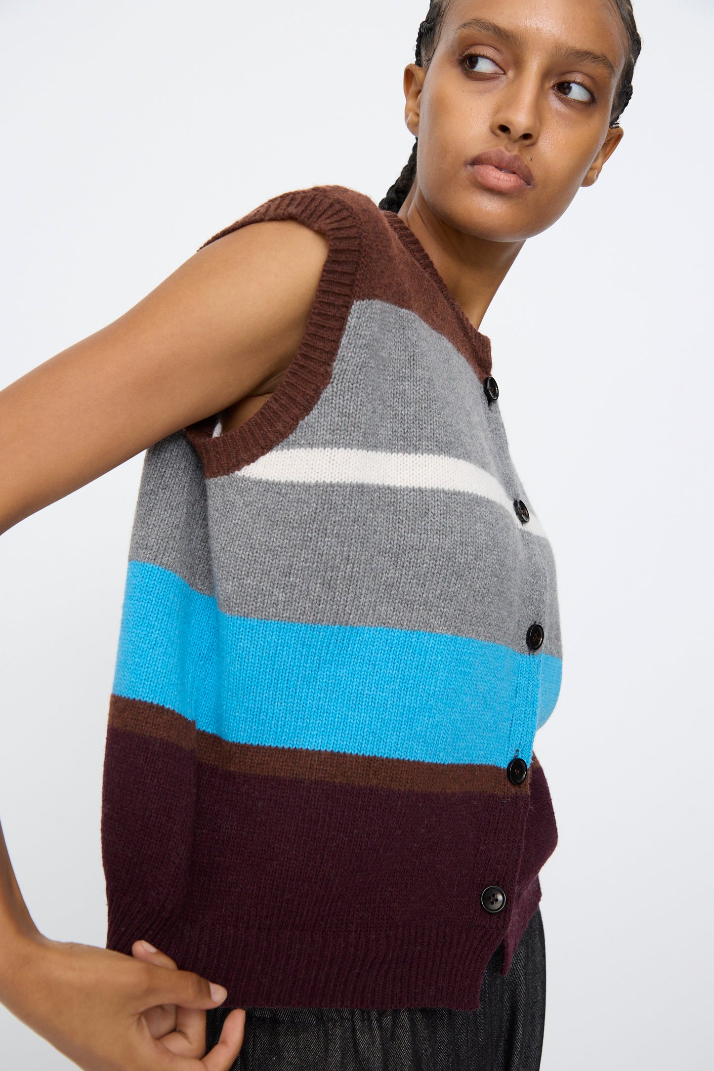 Someone wearing the AVN Funky Vest in Multicolor—a sleeveless, button-up wool blend vest with brown, gray, white, blue, and burgundy stripes made in Italy—paired with black pants.
