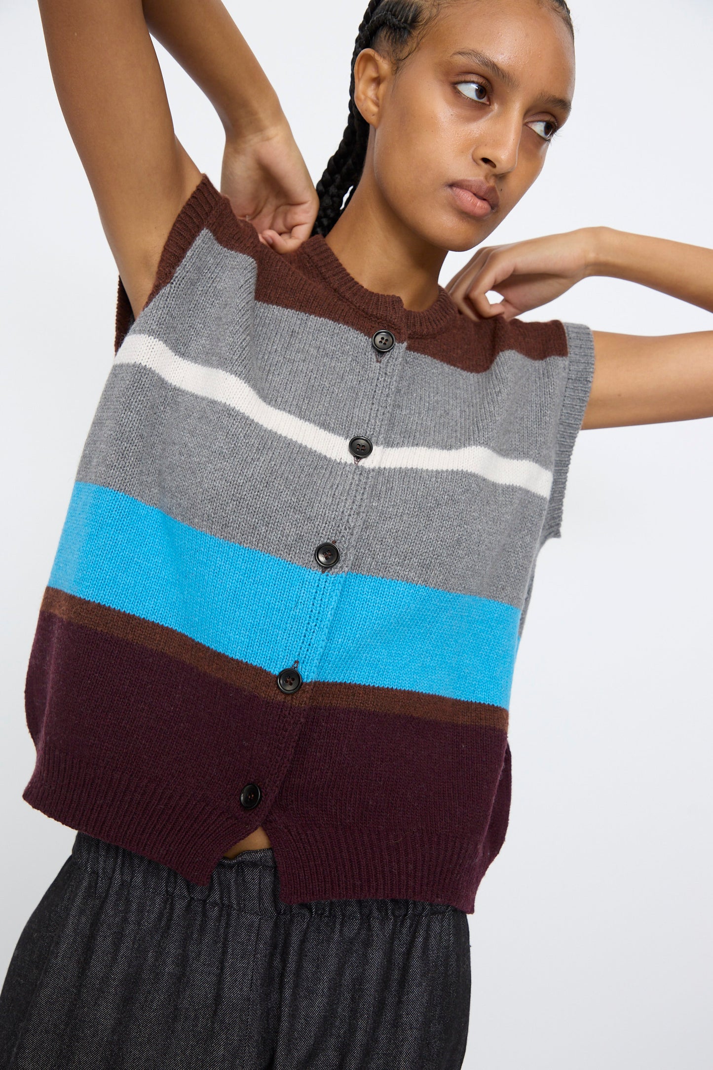 A person wearing the AVN Funky Vest in Multicolor—a sleeveless, button-up vest with brown, grey, white, blue, and burgundy horizontal stripes—paired with dark pants stands against a plain background.