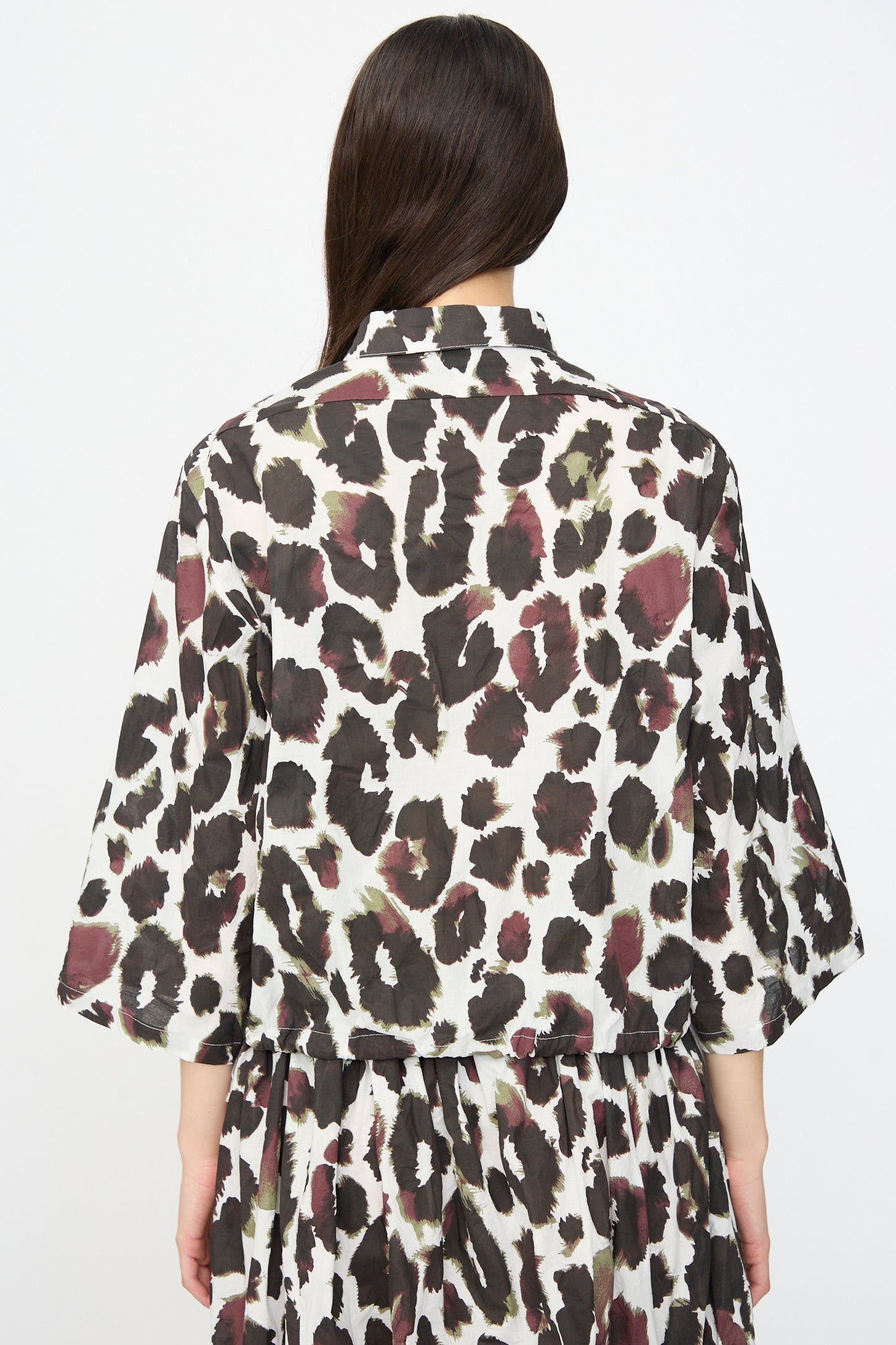 A person with long brown hair is shown from the back wearing the AVN Joyeux Top in White with Print, a loose-fitting, 3/4 sleeve animal print blouse featuring black, brown, and white spots.