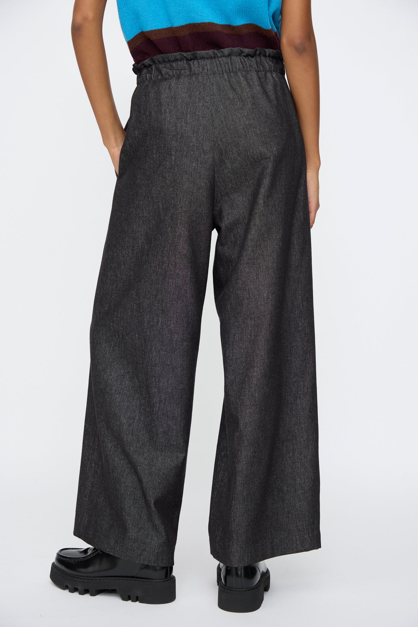 Model wearing AVN Long Easy Pants in Navy, featuring an elasticated waistband, paired with black shoes and a sleeveless striped top; shown from the back.