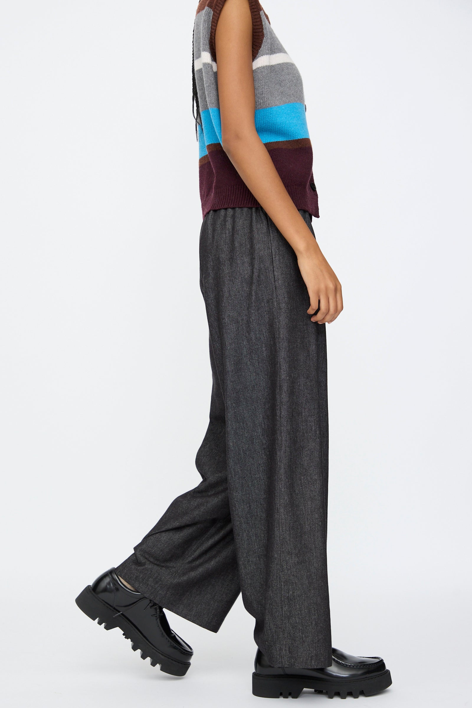 A person in a sleeveless striped sweater, AVN Long Easy Pants in Navy with an elasticated waistband, and black platform shoes, shown in side profile against a plain background.