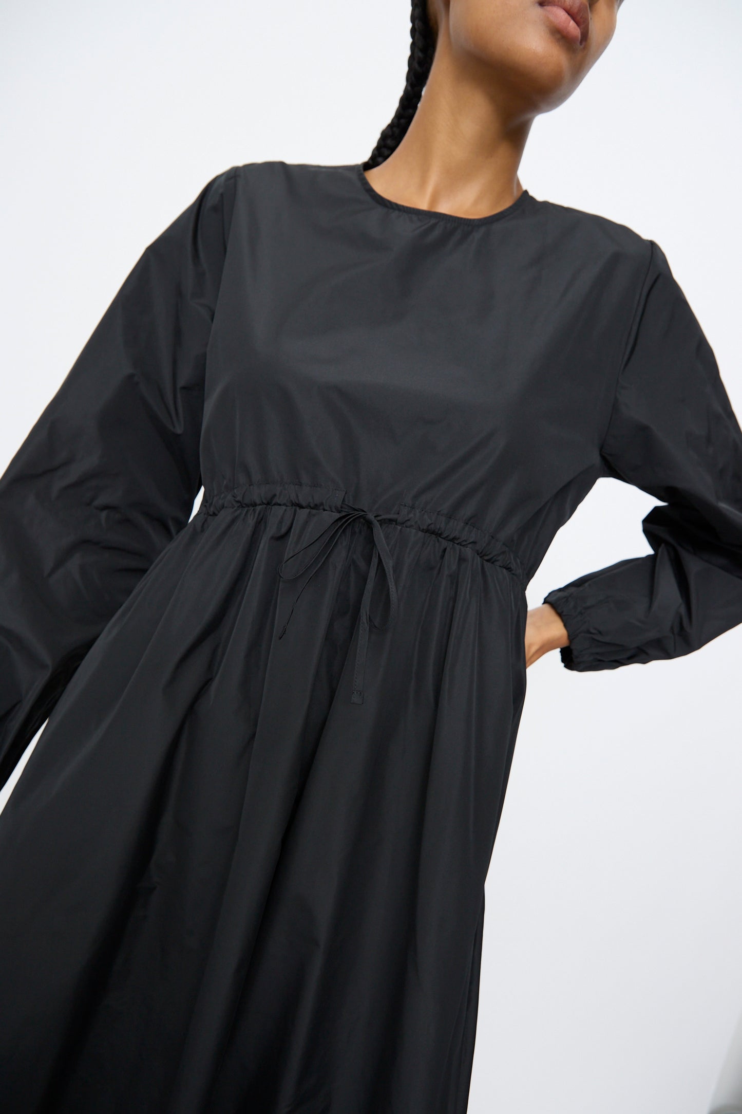 A person models the AVN New Gem Dress in Black, featuring bishop sleeves and an adjustable tie waist, against a plain light background.
