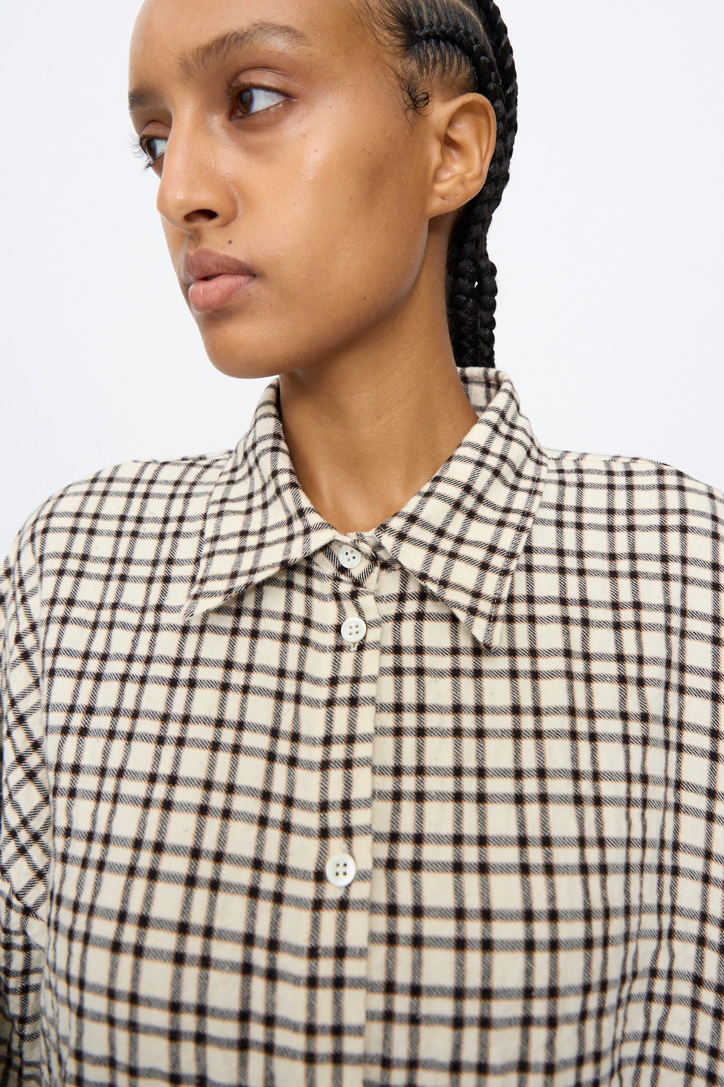 A person with braided hair wears the AVN Over Shirt in White and Black Check, looking to the side against a plain background.