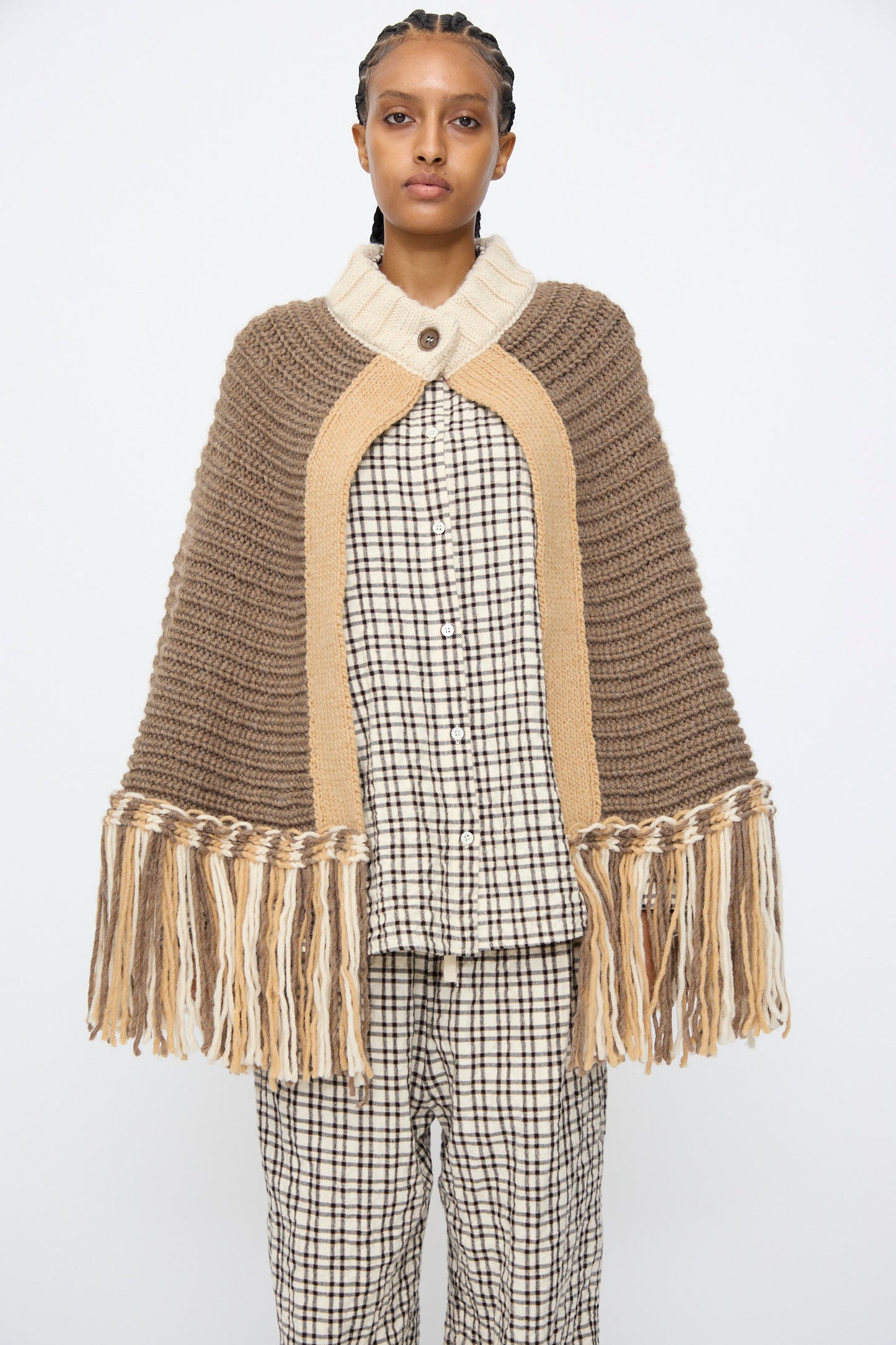 A person wears the AVN Peru Poncho in Brown and Beige Placket over a black-and-white checkered shirt and pants, standing against a plain white background.