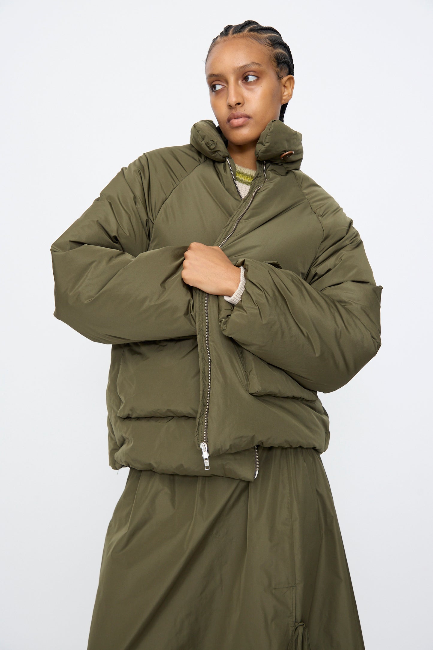 A person wearing the AVN Piumino Jacket in Military Green with an oversized fit and a matching skirt stands against a plain white background.