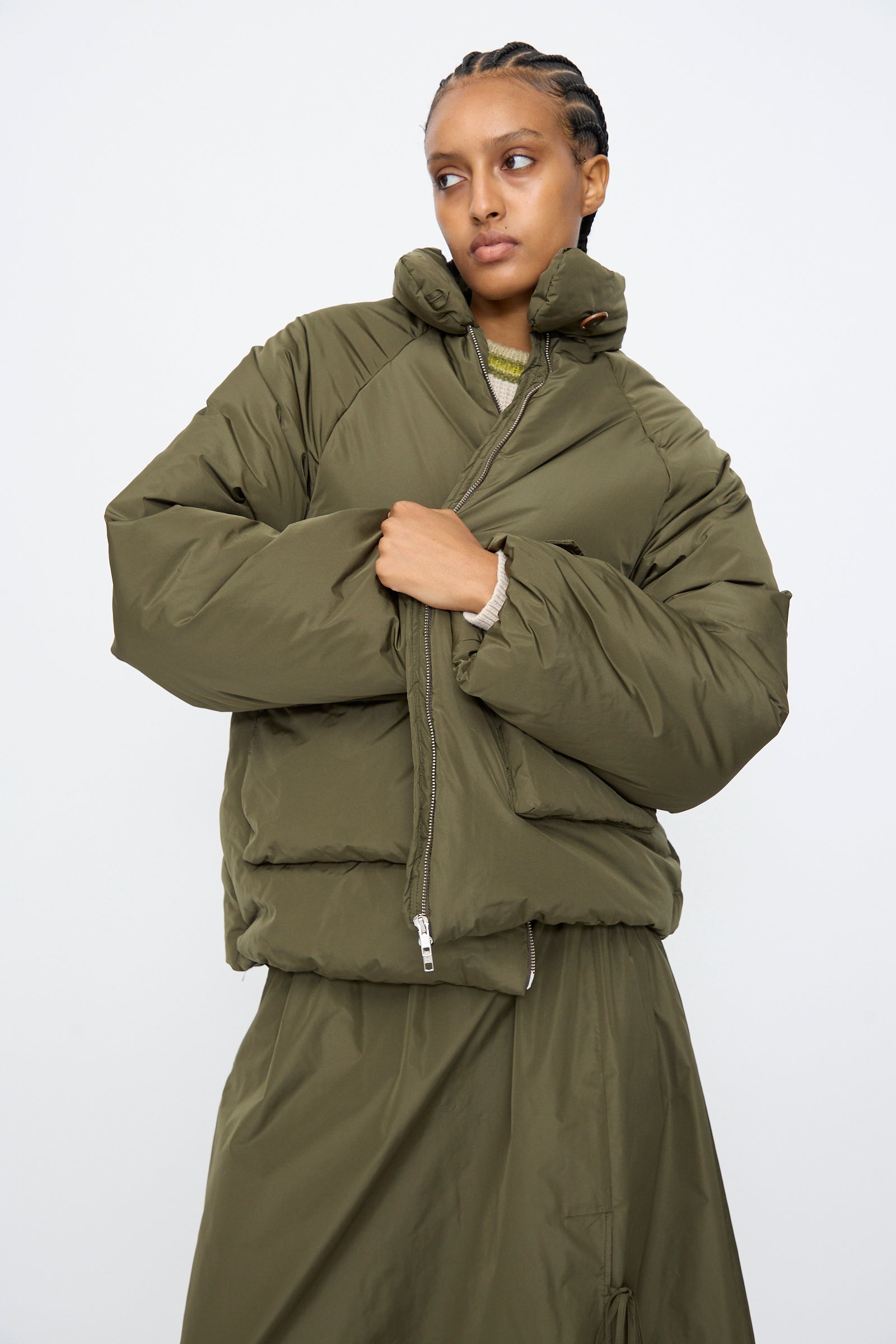 A person wearing the AVN Piumino Jacket in Military Green with an oversized fit and a matching skirt stands against a plain white background.