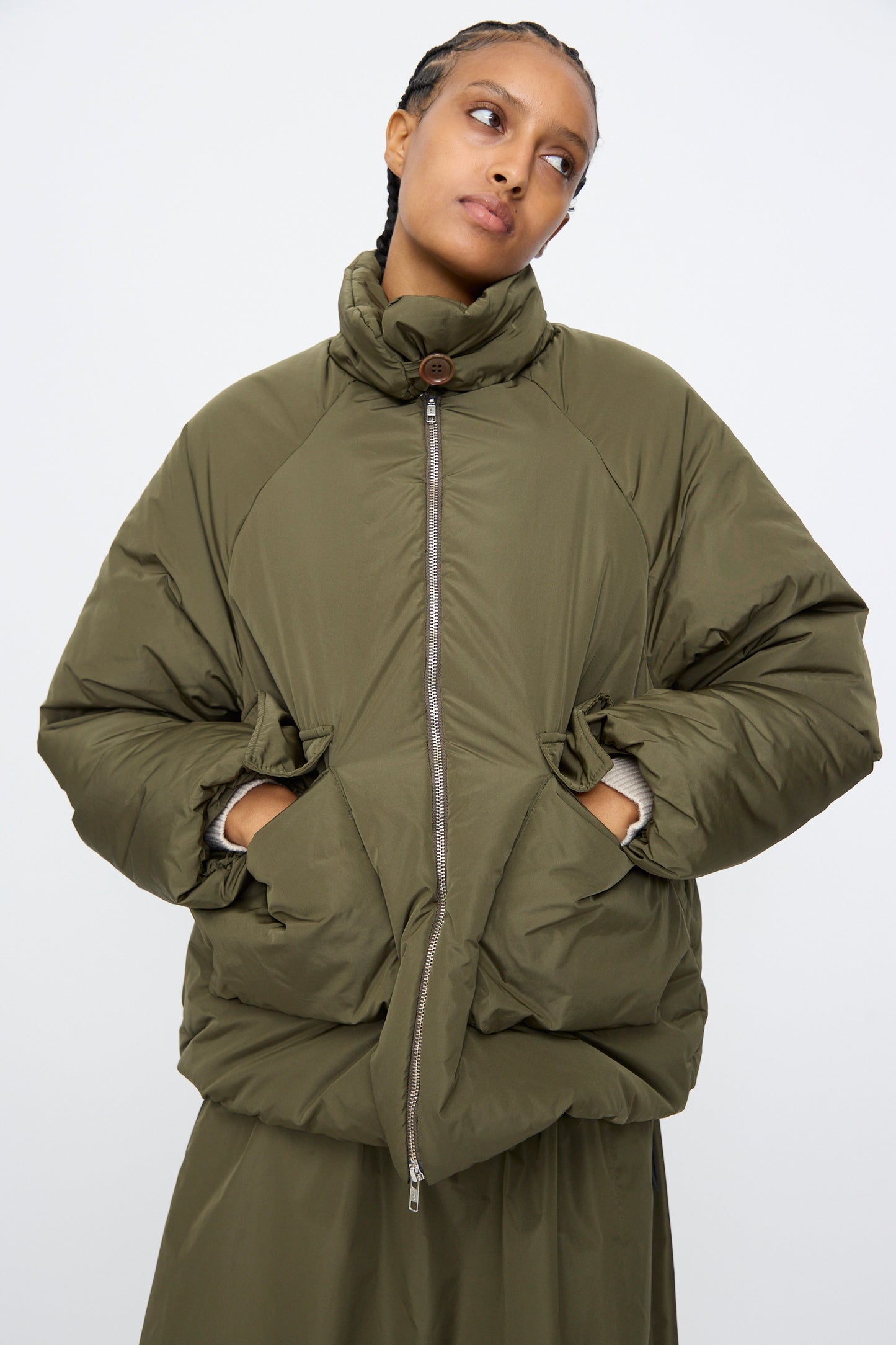 Someone wears the AVN Piumino Jacket in Military Green, styled in an oversized fit with hands in pockets, posed against a plain light background.