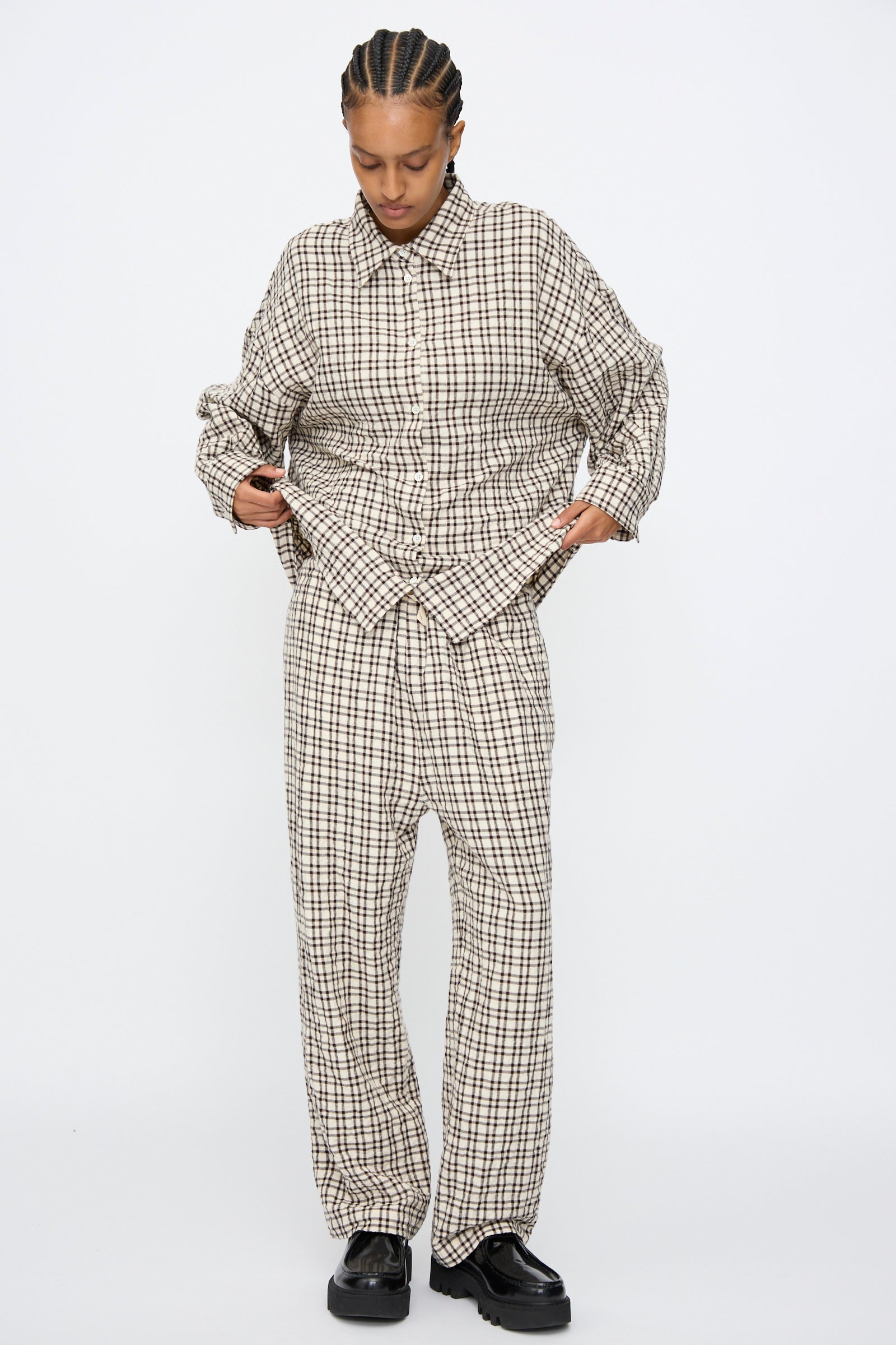 A person wears AVN's Pj Pants in White and Black Check, paired with a matching shirt and black shoes, standing against a plain white background.