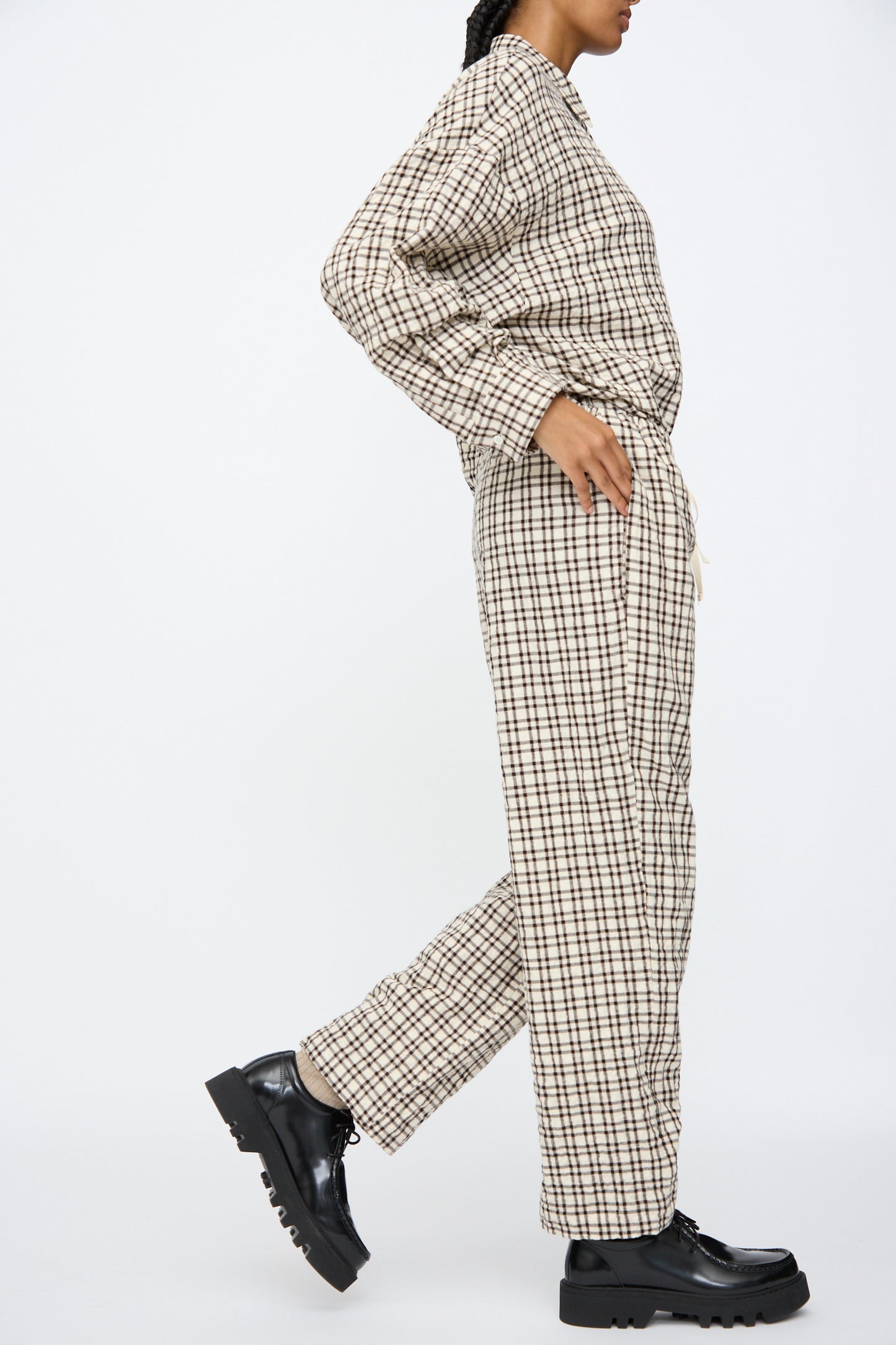 Wearing AVN Pj Pants in White and Black Check, paired with black platform shoes, the person stands with one foot slightly forward against a plain white background.