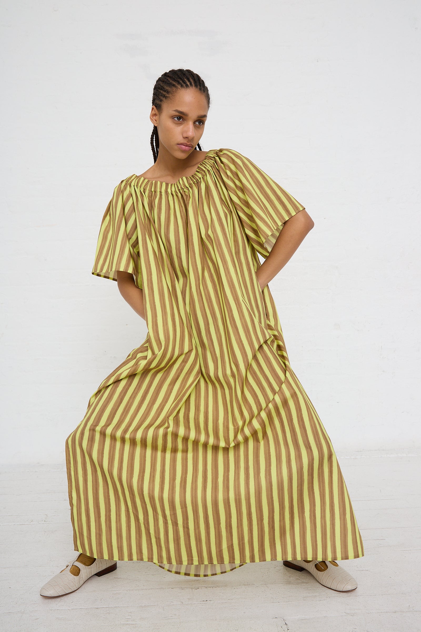 A woman in a AVN striped yellow and green Italian womenswear collection cotton maxi dress with oversized short sleeves posing against a white background.
