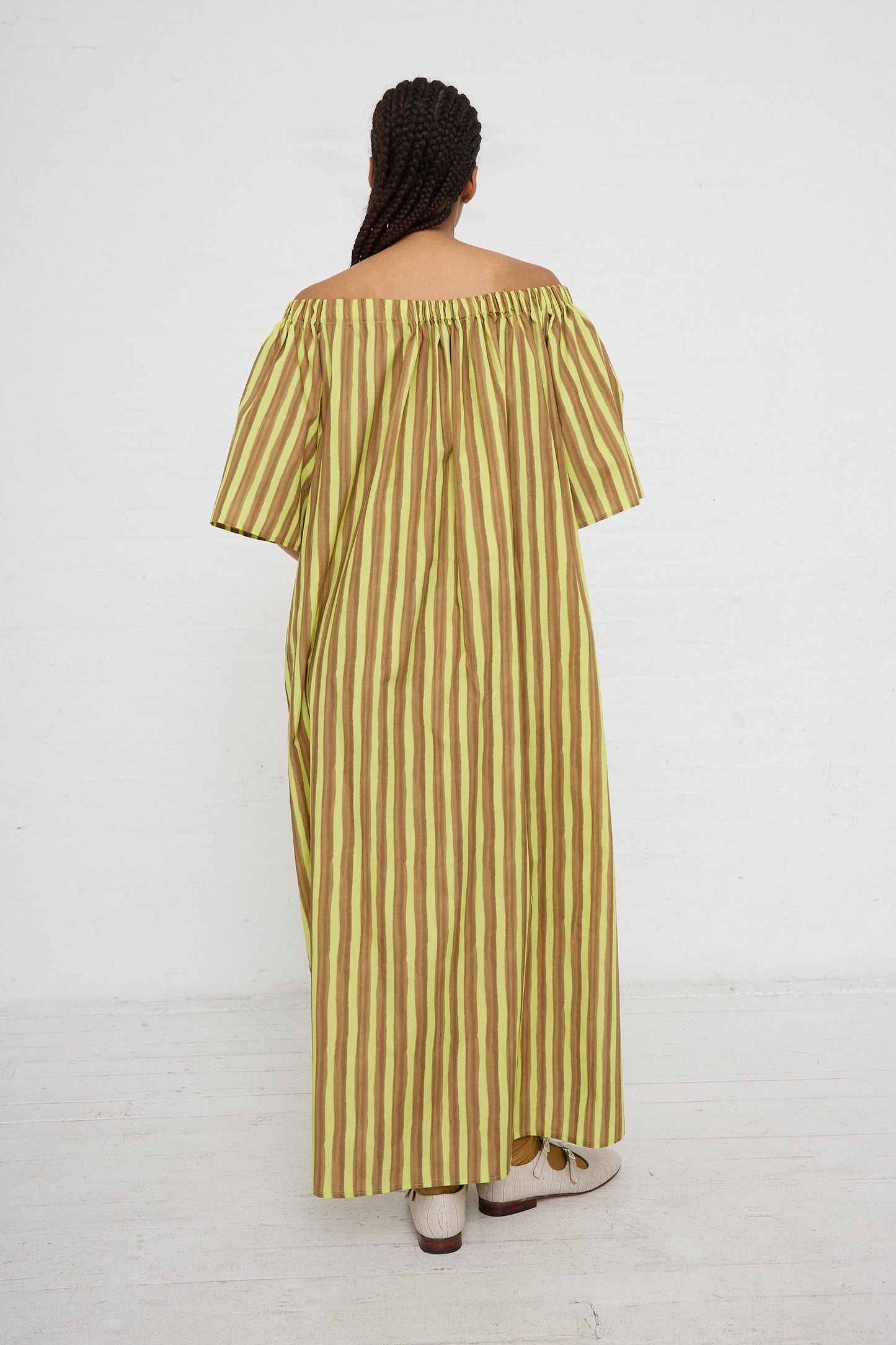 Sentence with replaced product: A person standing with their back to the camera, wearing a AVN striped cotton maxi dress with oversized short sleeves and brown shoes.