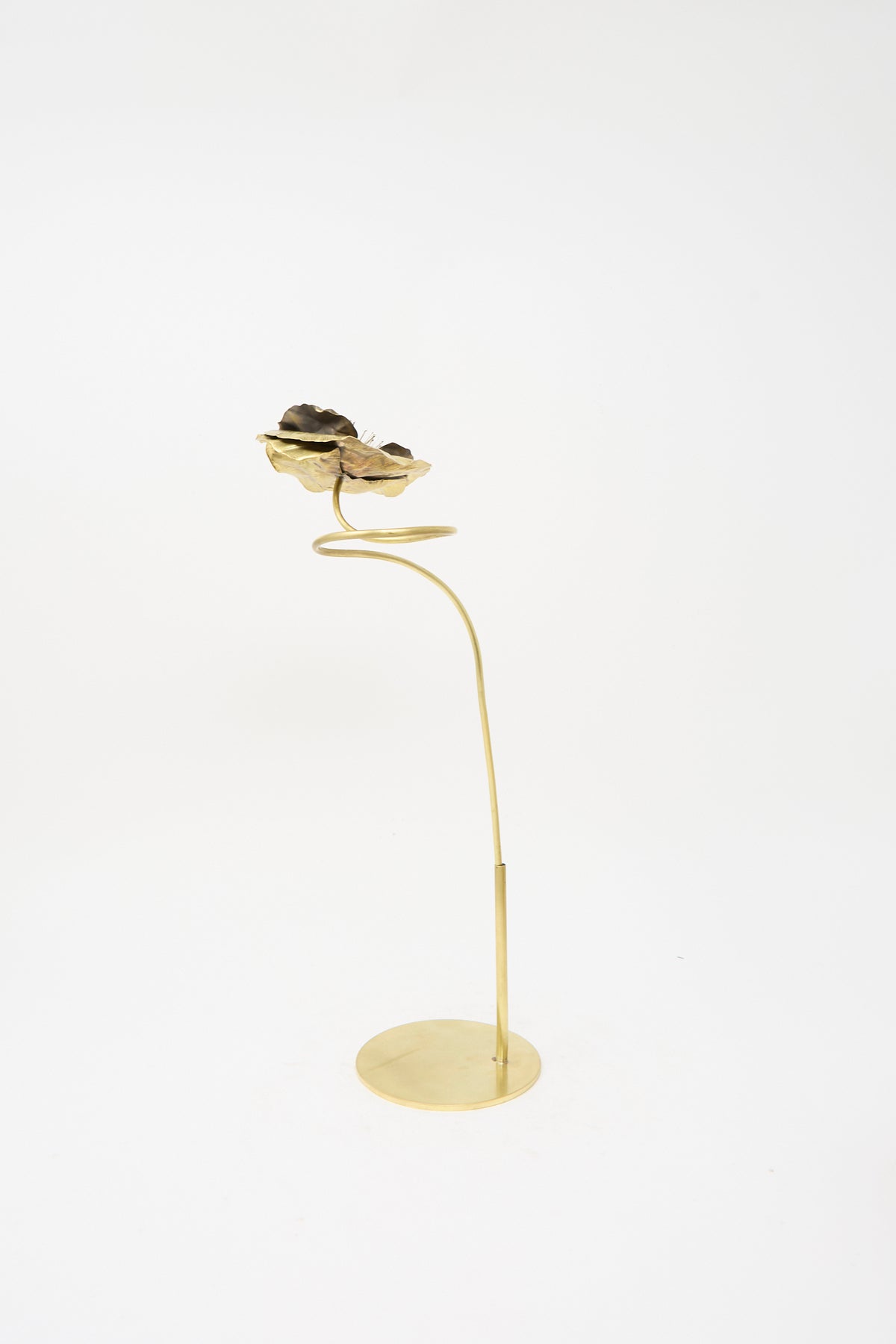 An Alison Layton Sterling Silver and Brass Papaver No. 7 - I sculpture featuring a thin brass stem rising from a circular base, topped with a dark, textured flower-shaped accent.