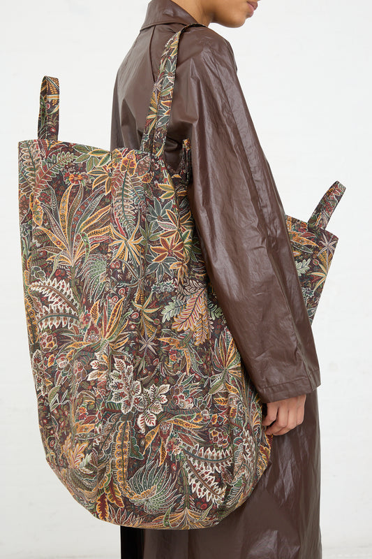 A person wearing a brown coat carries a large Amiacalva Easy Bag in Liberty Khaki cotton shoulder bag.