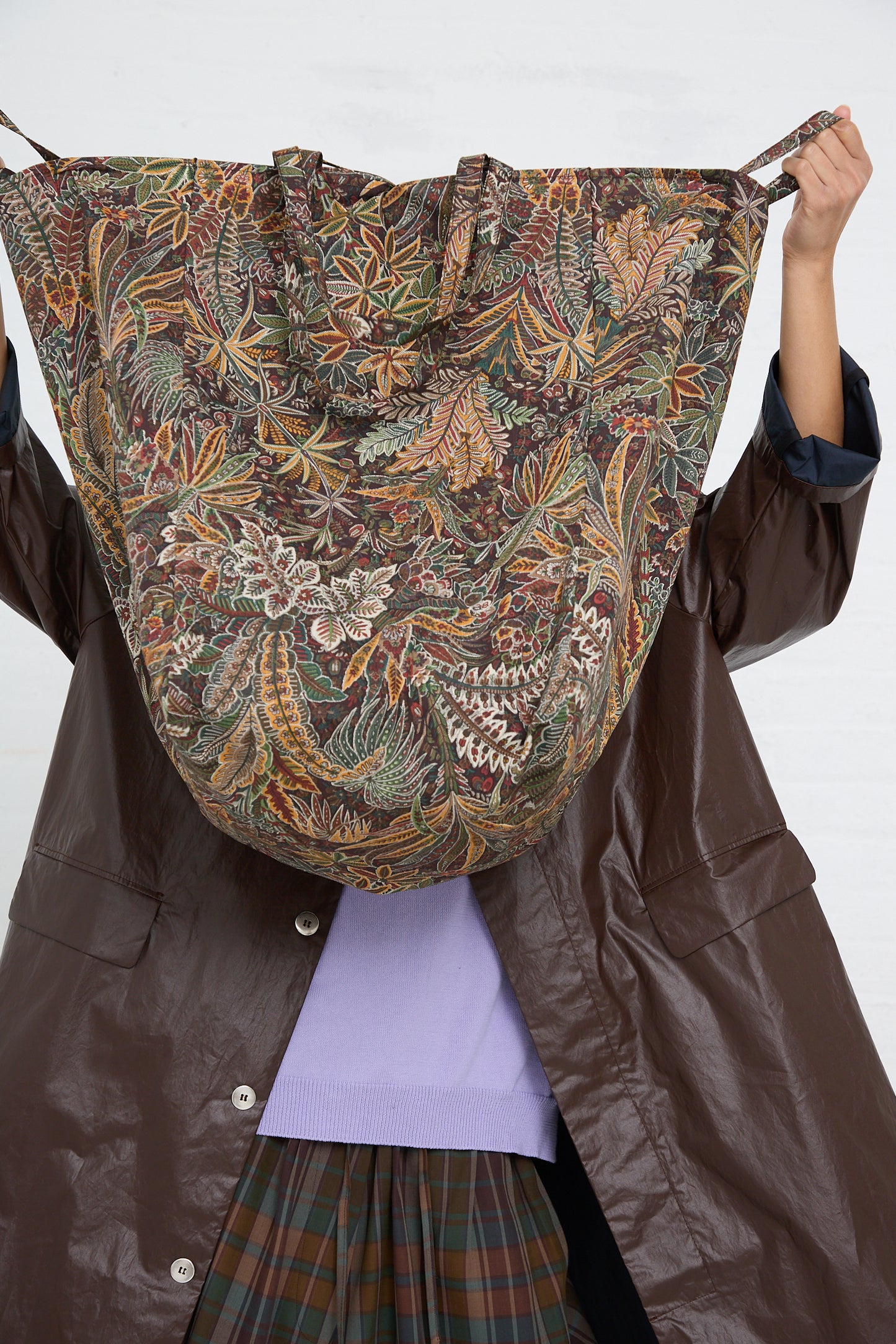 Person holding up an Amiacalva Easy Bag in Liberty Khaki print cotton decorative fabric with a leafy pattern in front of their face.