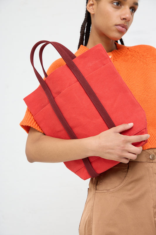 A person holding an Amiacalva Light Ounce Canvas Tote in Scarlet and Burgundy over their shoulder.