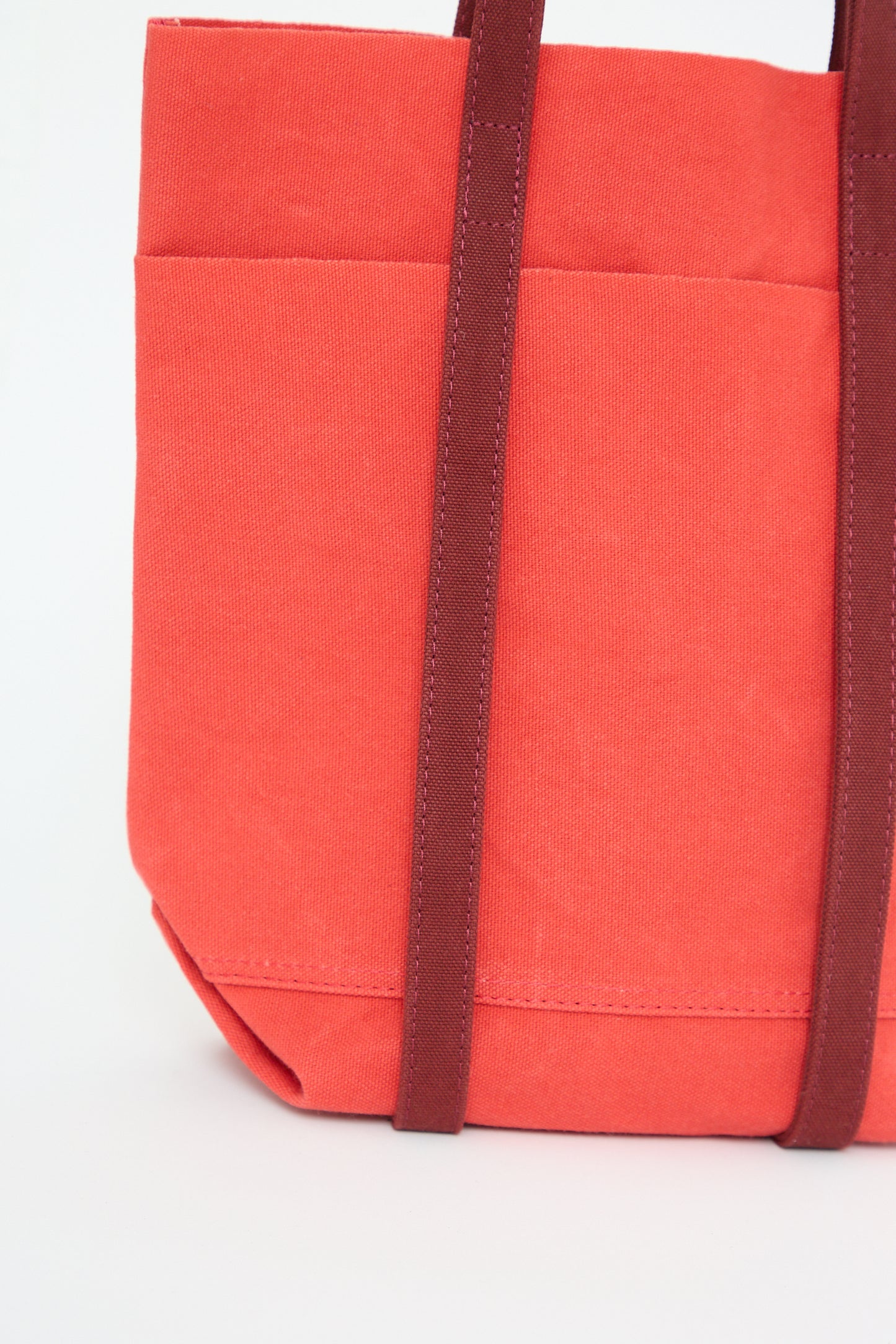 A close-up of a red Amiacalva Light Ounce Canvas Tote in Scarlet and Burgundy with brown handles against a white background.