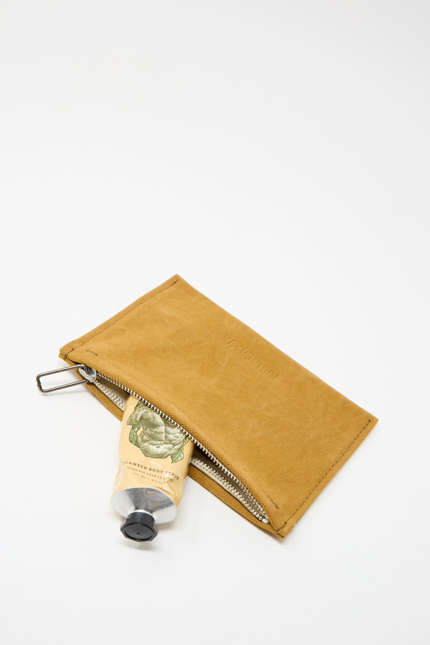 The Amiacalva Washed Canvas Medium Pouch in Mustard, partially open with a tube of hand cream inside, rests on a white background.