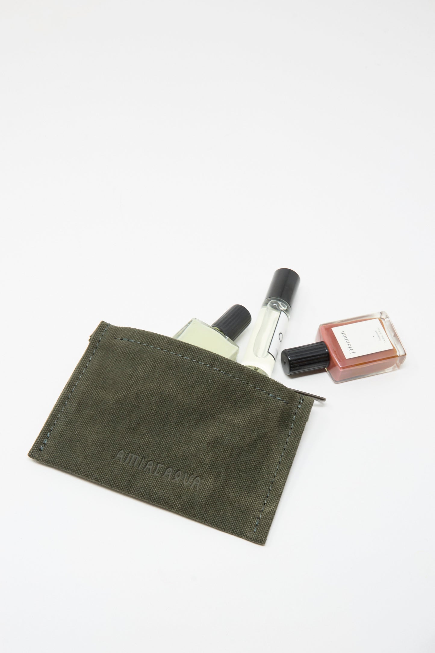 The Amiacalva Washed Canvas Small Pouch in Olive, made in Japan, features a zipper top and holds three small perfume bottles—two clear glass and one amber—partially visible against a white background.