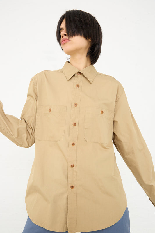 A woman with a short dark bob hairstyle wearing an As Ever beige button-down shirt in 40's Khaki with two chest pockets, posing against a white background.