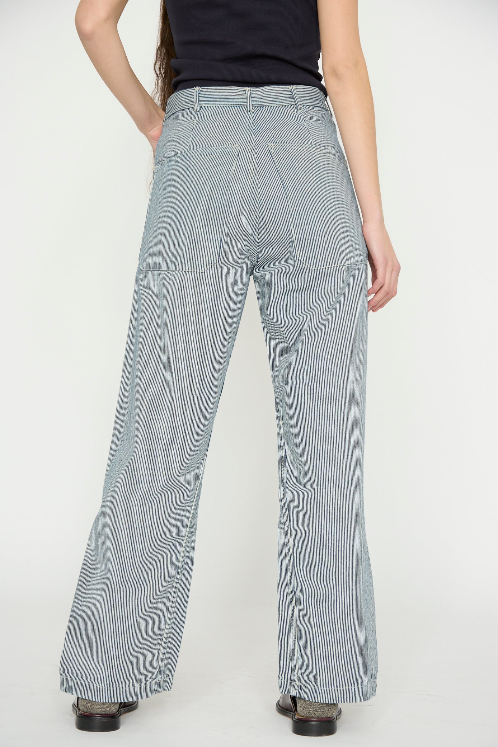 Rear view of a person in the As Ever black top and Brancusi Pant in Engineer Stripe, showcasing a wide-leg silhouette inspired by 1940s vintage style, against a plain background.