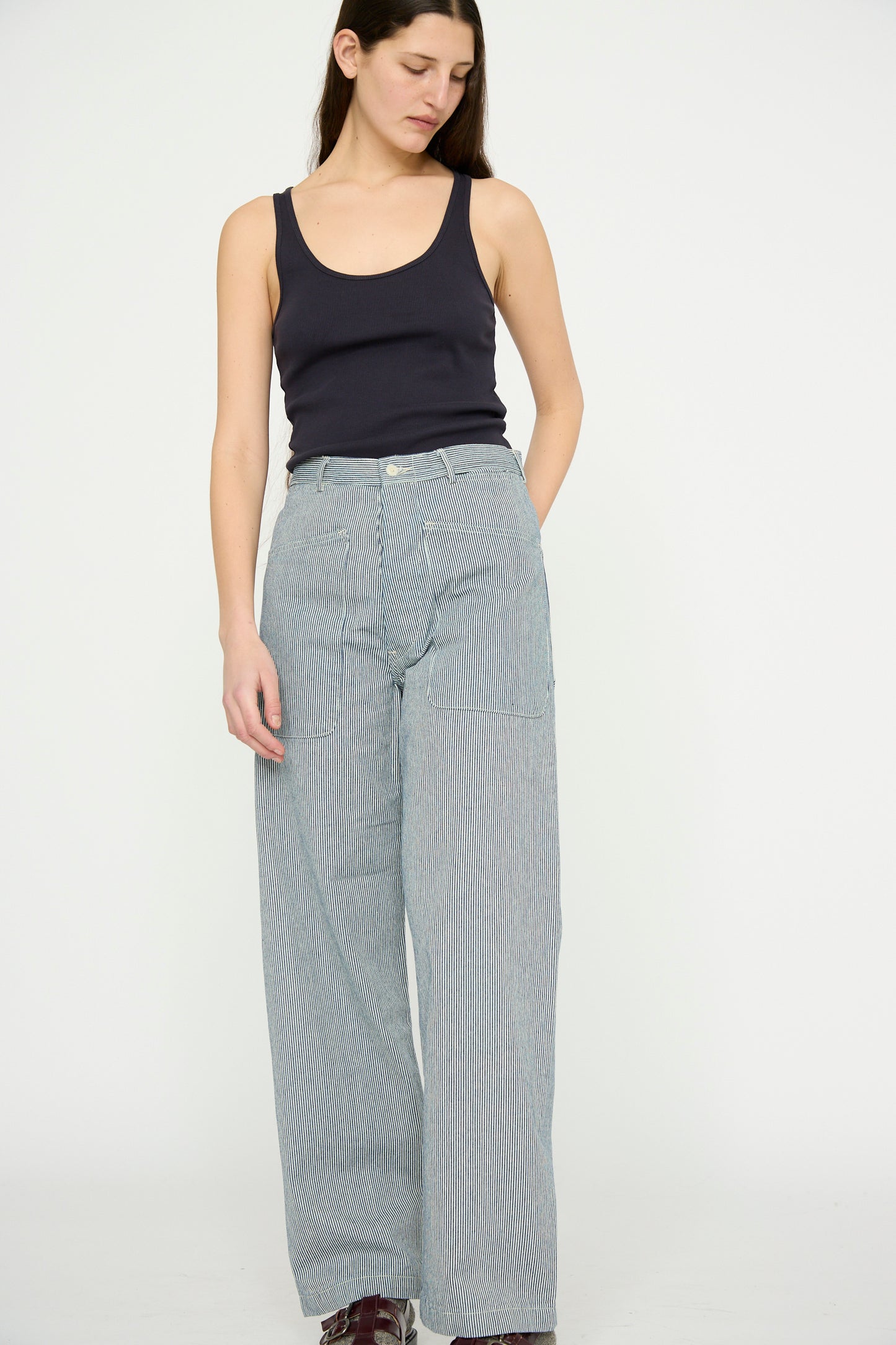 A person in a black tank top and Brancusi Pant in Engineer Stripe by As Ever, inspired by 1940s vintage style, stands against a plain background.