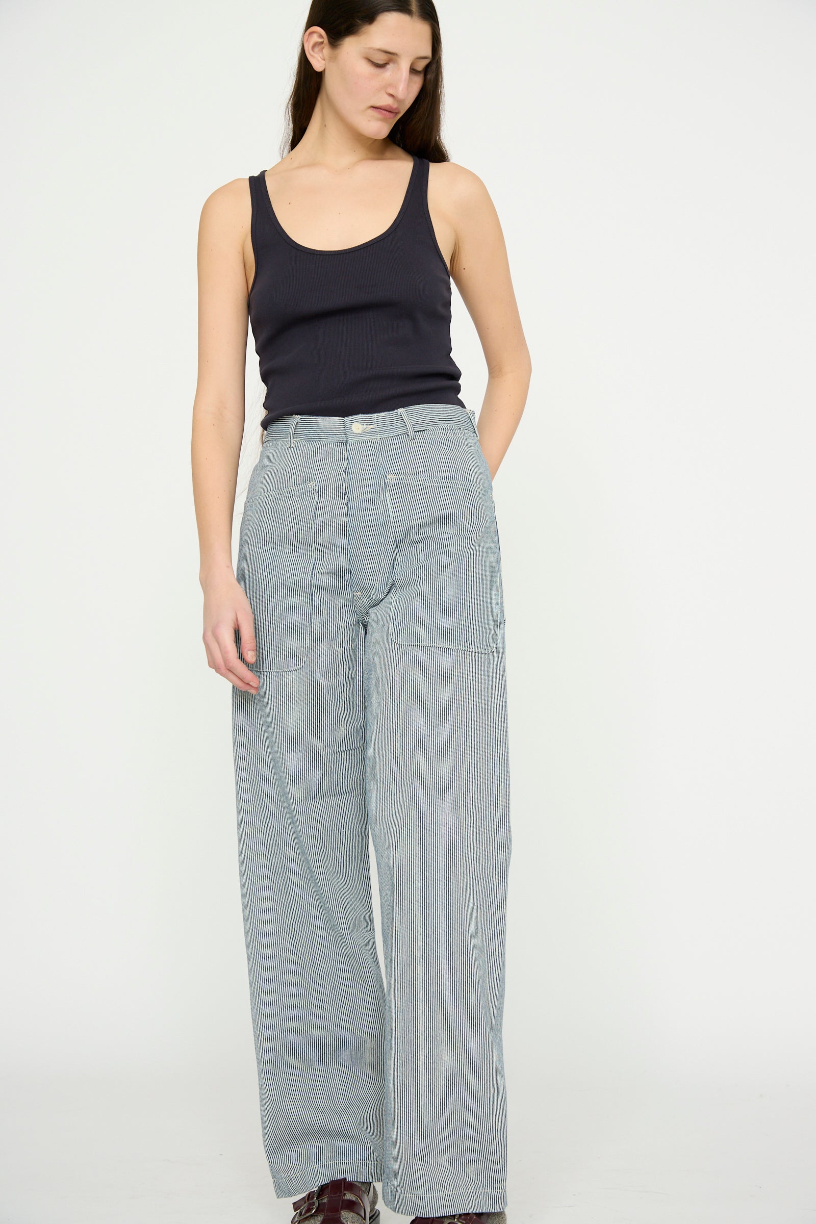A person in a black tank top and Brancusi Pant in Engineer Stripe by As Ever, inspired by 1940s vintage style, stands against a plain background.