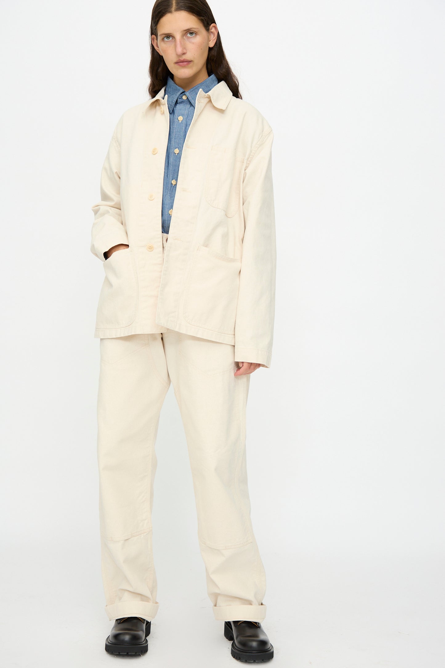 A person wears the As Ever Henri Jacket in Natural with matching pants, a blue button-up shirt, and black shoes, standing against a plain white background.