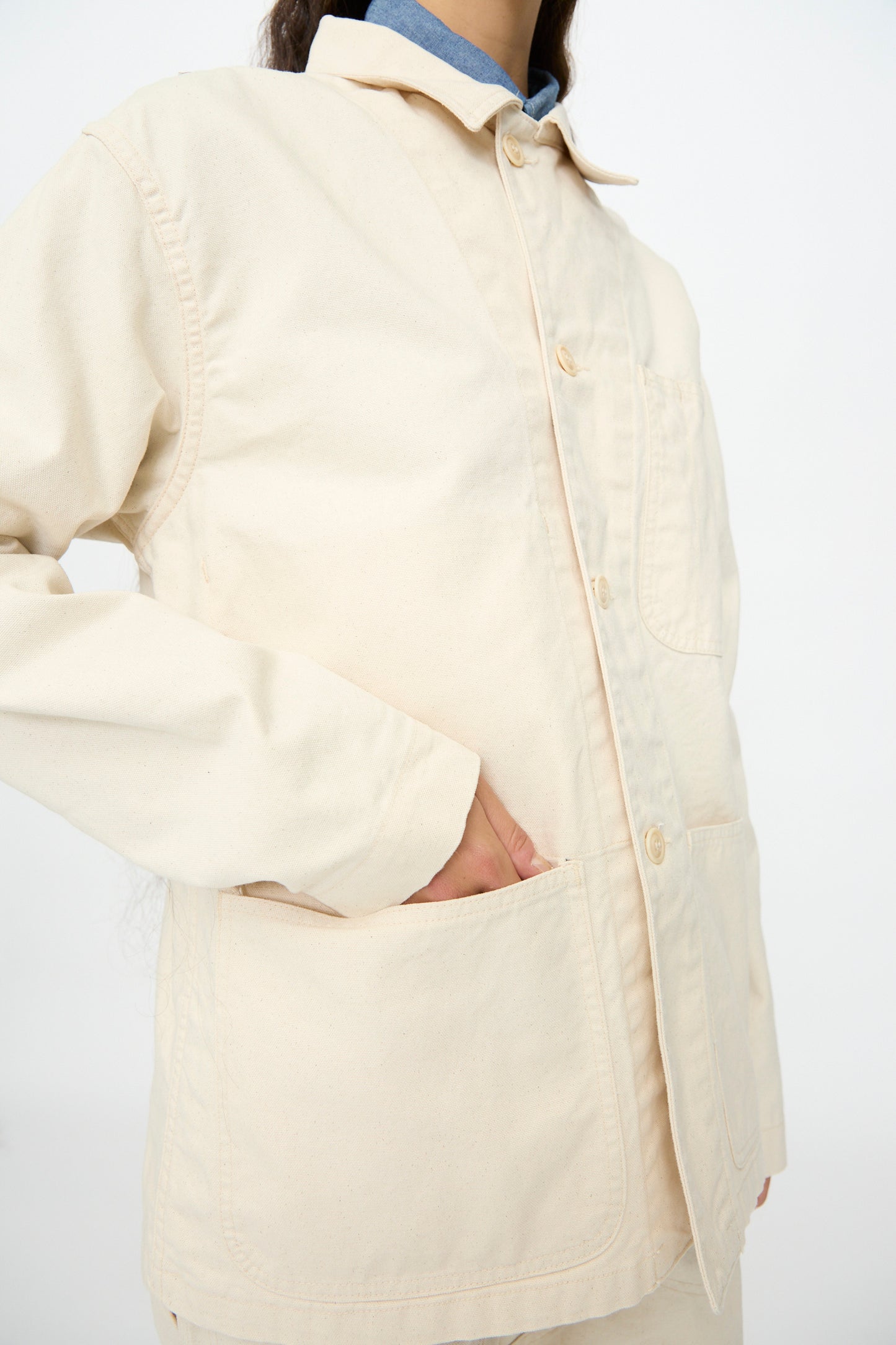 A person wears the Henri Jacket in Natural by As Ever, with one hand in a front pocket, posing against a plain white background.