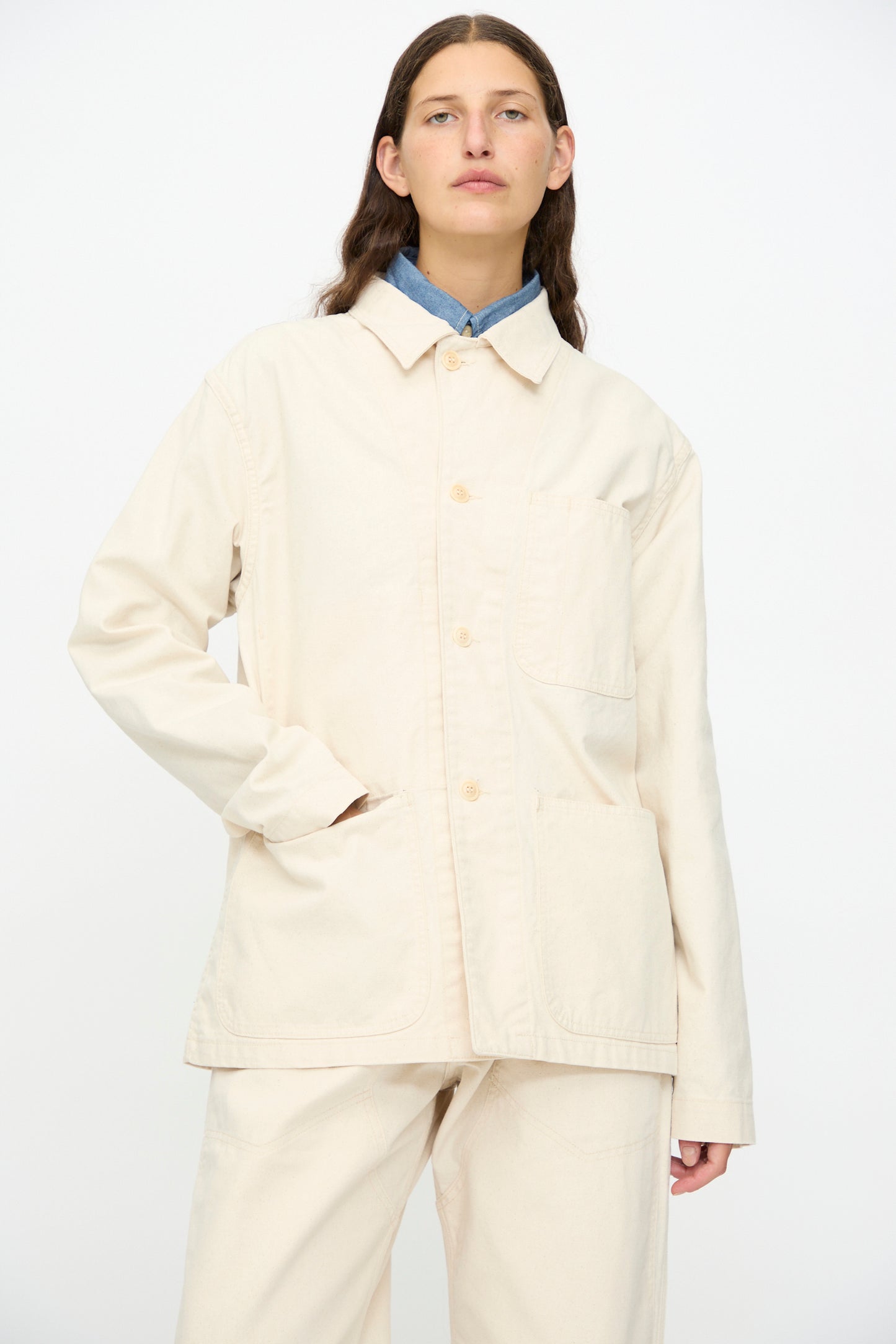 A person wears the As Ever Henri Jacket in Natural with matching pants, one hand in the jacket pocket, posing against a plain white background.