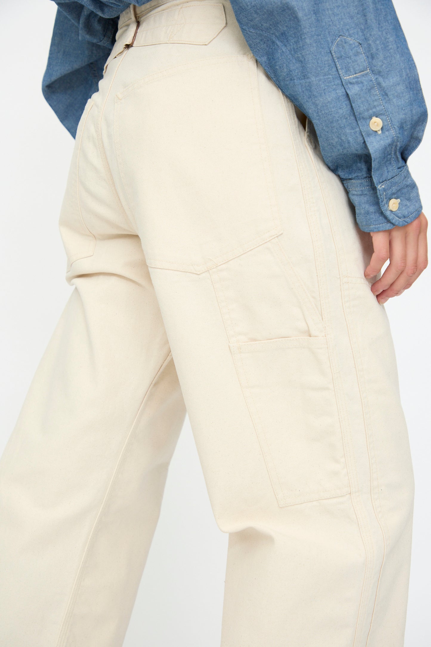 Person wearing a blue long-sleeve shirt and the Henri Pant in Natural by As Ever, styled as high-waisted wide-leg unbleached canvas with visible seams and a side pocket.