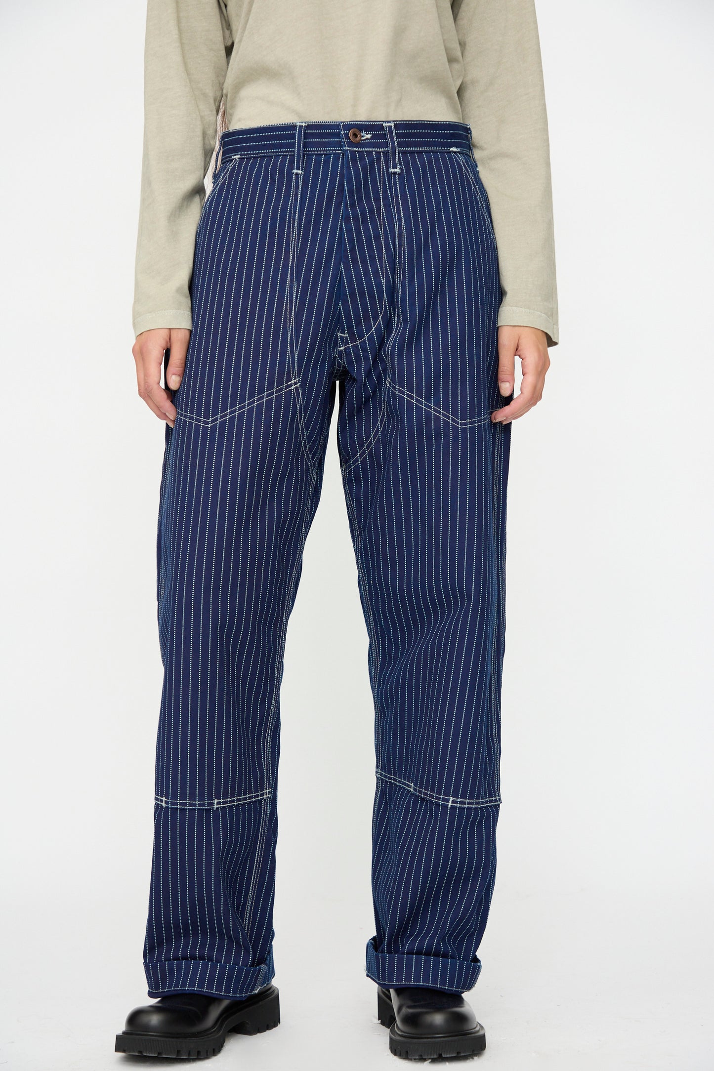 Person wearing the Henri Pant in Wabash by As Ever, paired with a light beige long-sleeve shirt and black shoes, standing against a plain white background.
