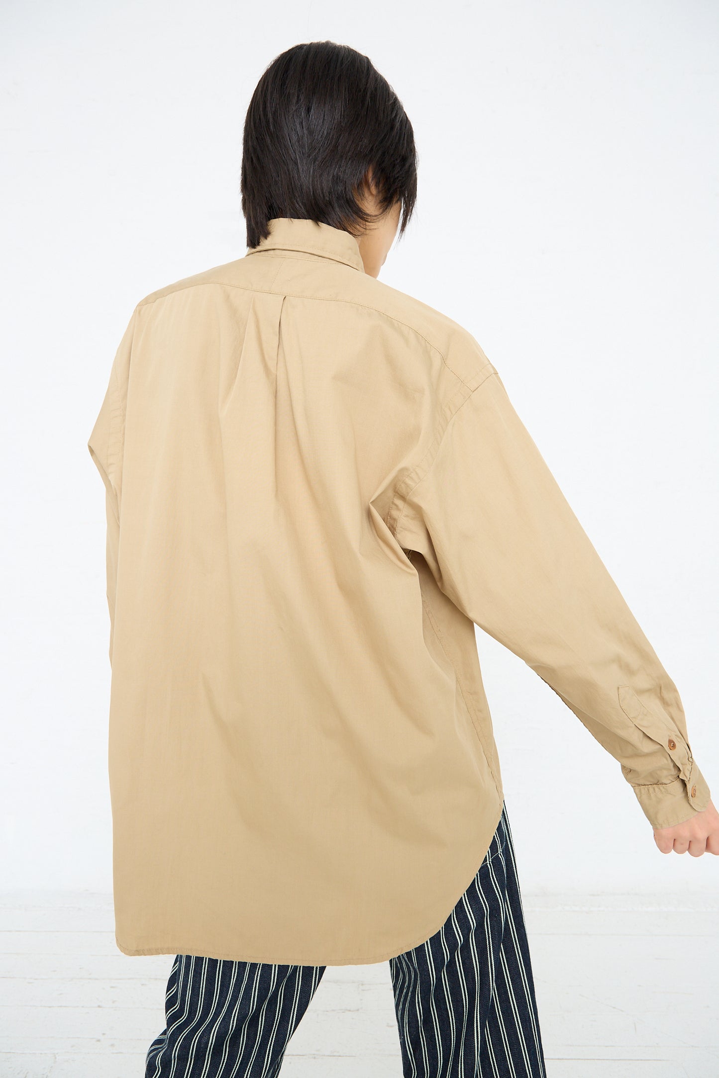 A person seen from the back wearing an oversized As Ever Largo Shirt in 40's Khaki and striped pants against a white background.