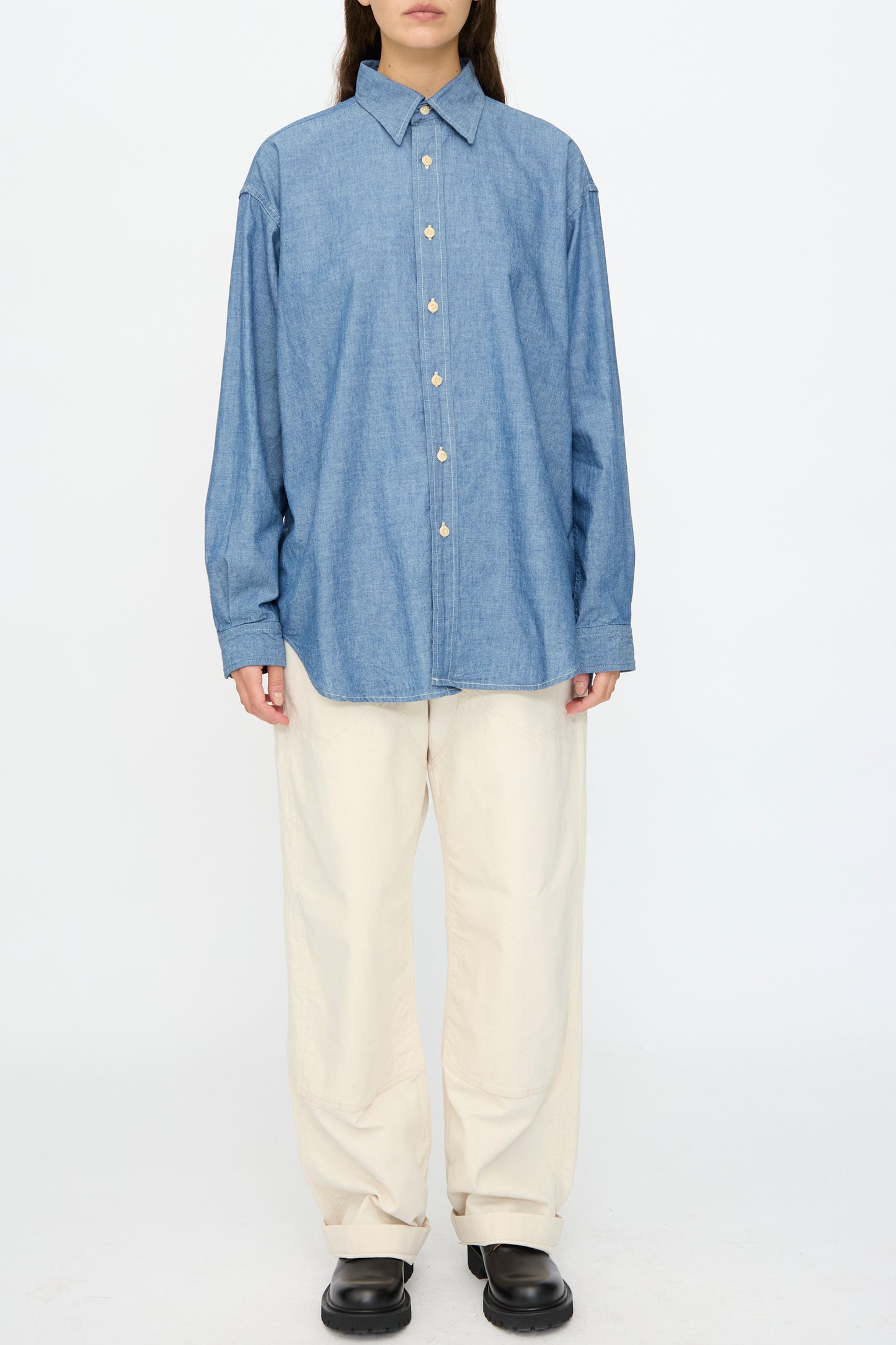 Model wearing the As Ever Largo Shirt in Chambray, paired with off-white wide-leg pants and black shoes, standing against a plain white background.