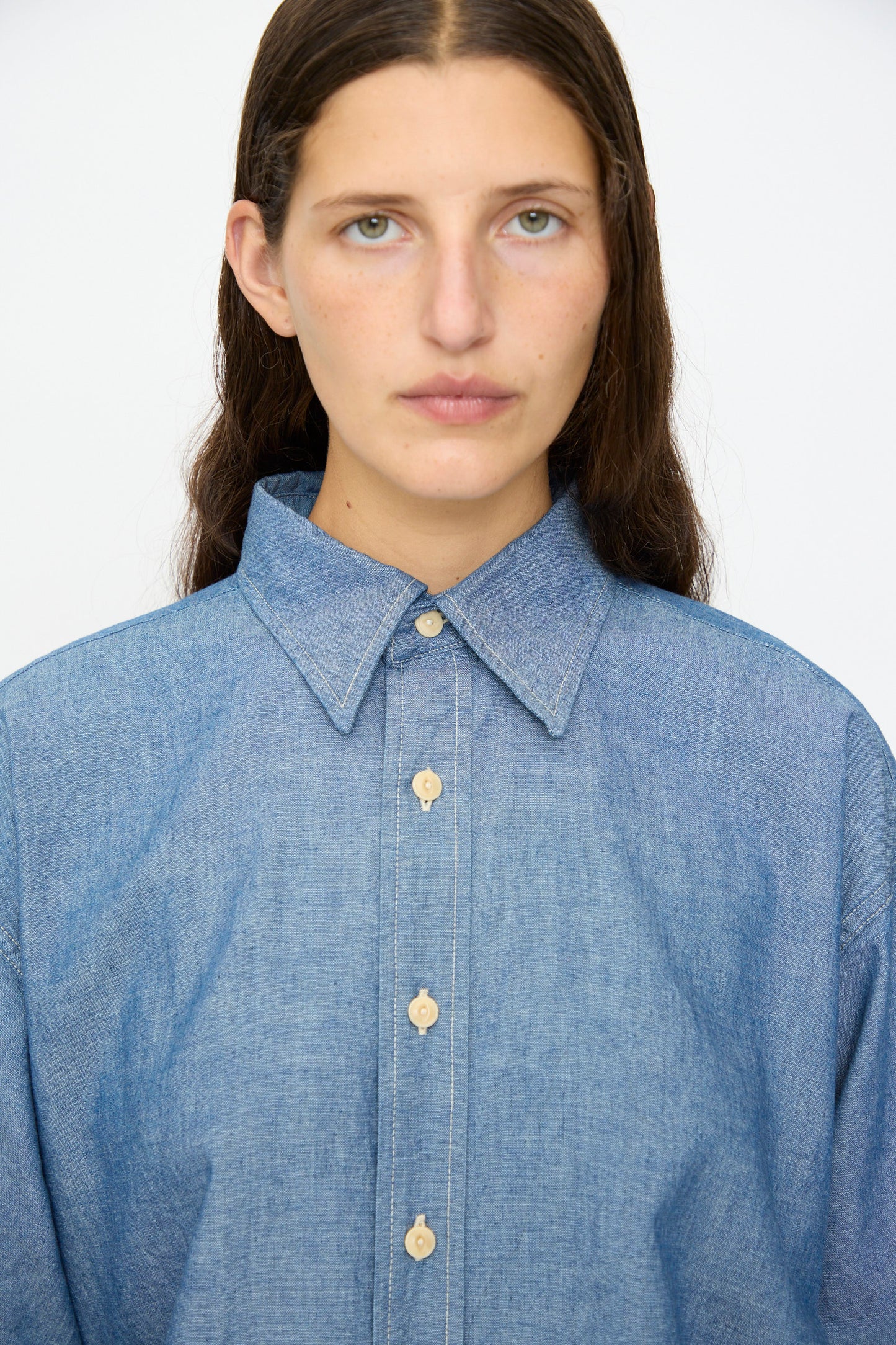 A person with long brown hair wears the As Ever Largo Shirt in Chambray, looking directly at the camera against a plain background.