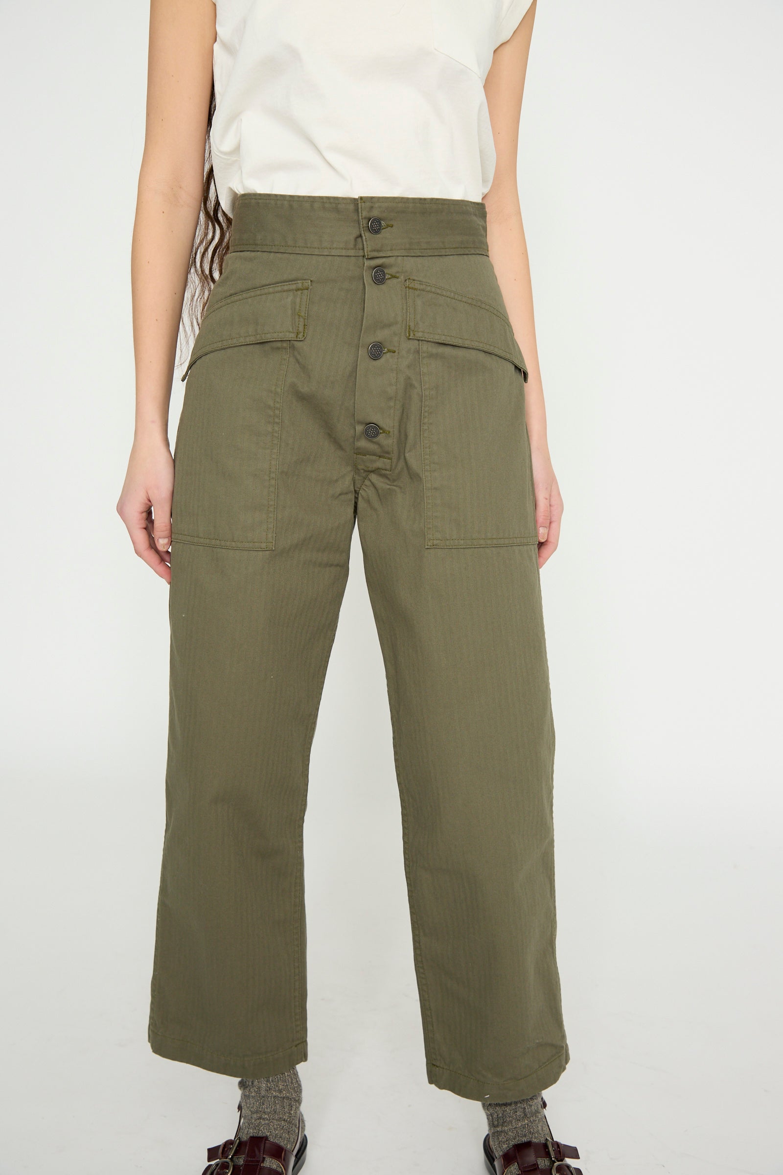 Person wearing As Ever's Tanker in Olive, wide-leg pants featuring a relaxed fit and front pockets, paired with a white top, standing against a plain background.