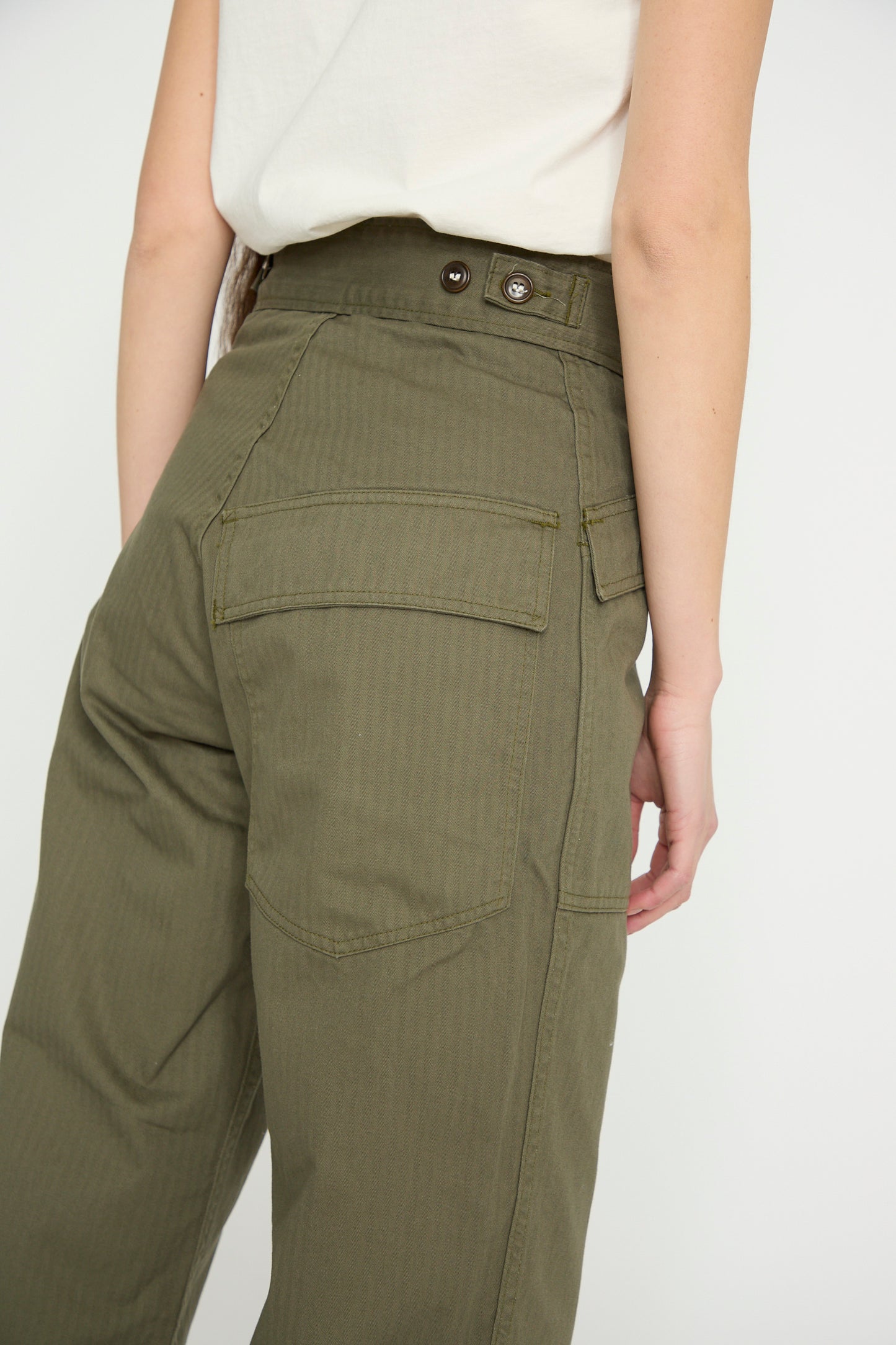 A person models the Tanker in Olive by As Ever, high-waisted with button details and large back pockets, viewed from behind against a white backdrop.