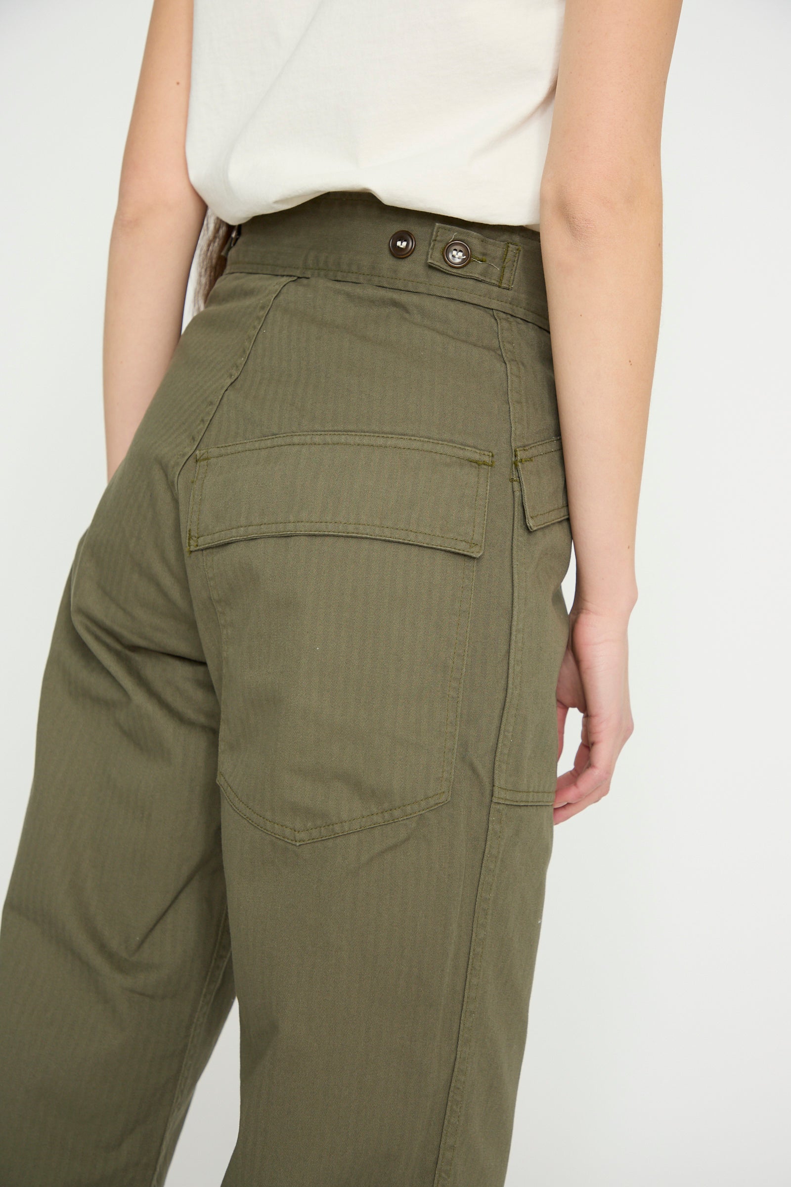 A person models the Tanker in Olive by As Ever, high-waisted with button details and large back pockets, viewed from behind against a white backdrop.