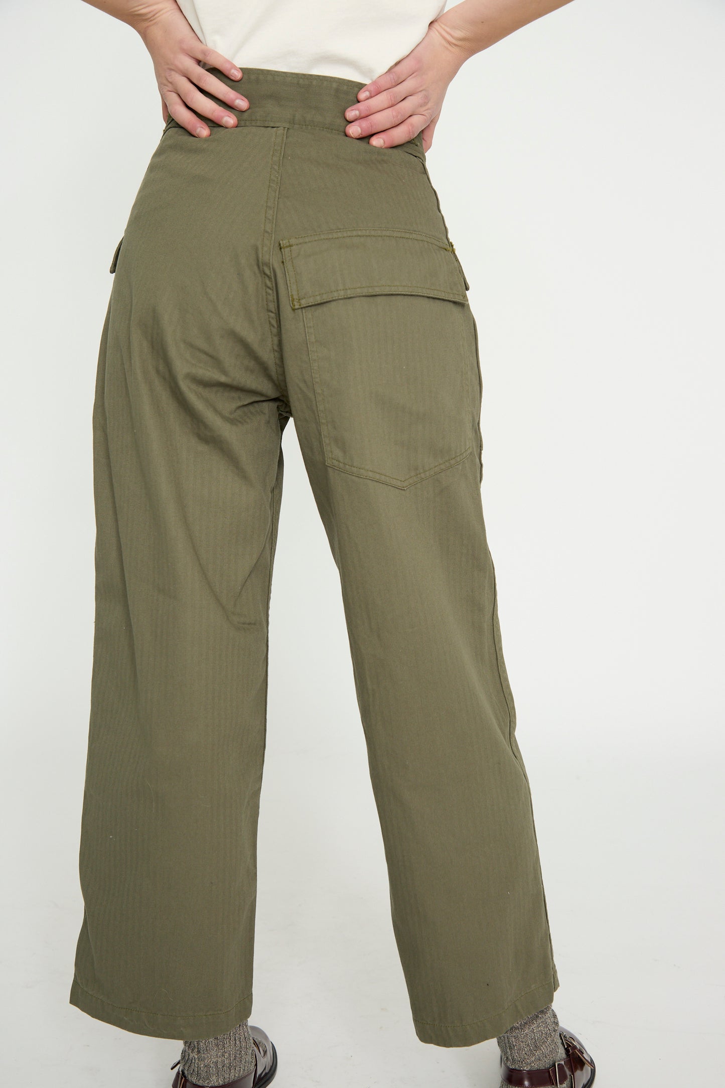 A person facing away wearing the Tanker in Olive, a relaxed fit cargo pants by As Ever, stands with hands on hips against a plain background.
