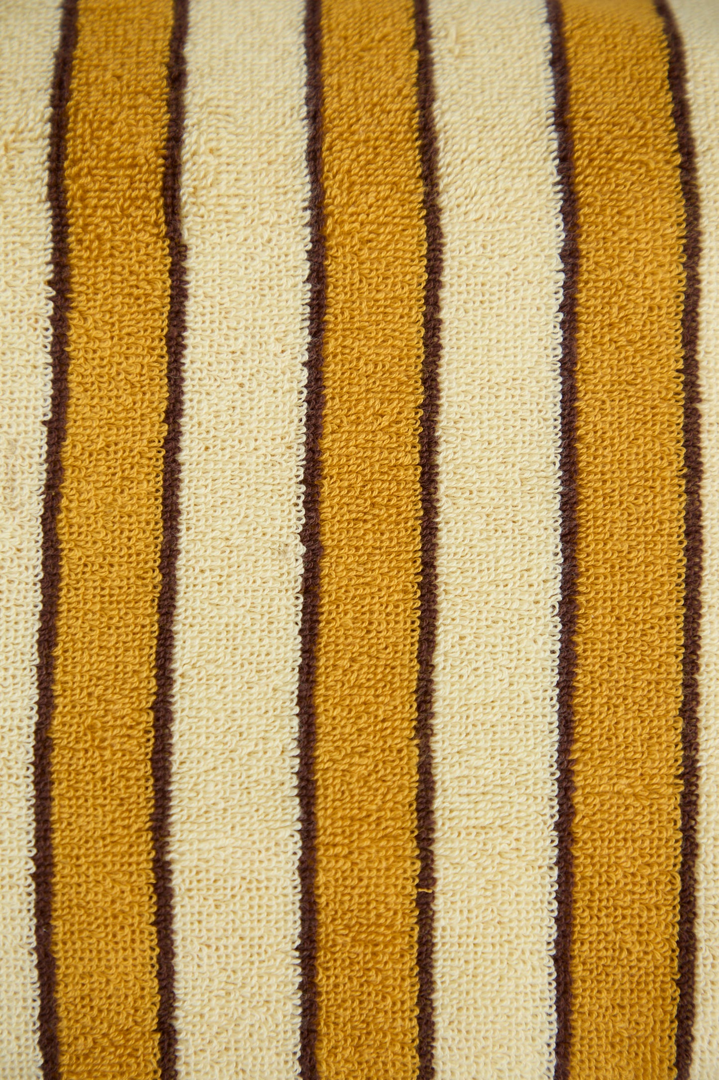A close-up of the Helena Pool Towel in Ochre by Autumn Sonata, featuring a textured pattern with alternating vertical stripes in mustard yellow, cream, and brown, inspired by traditional Edo textiles and crafted from soft organic cotton.