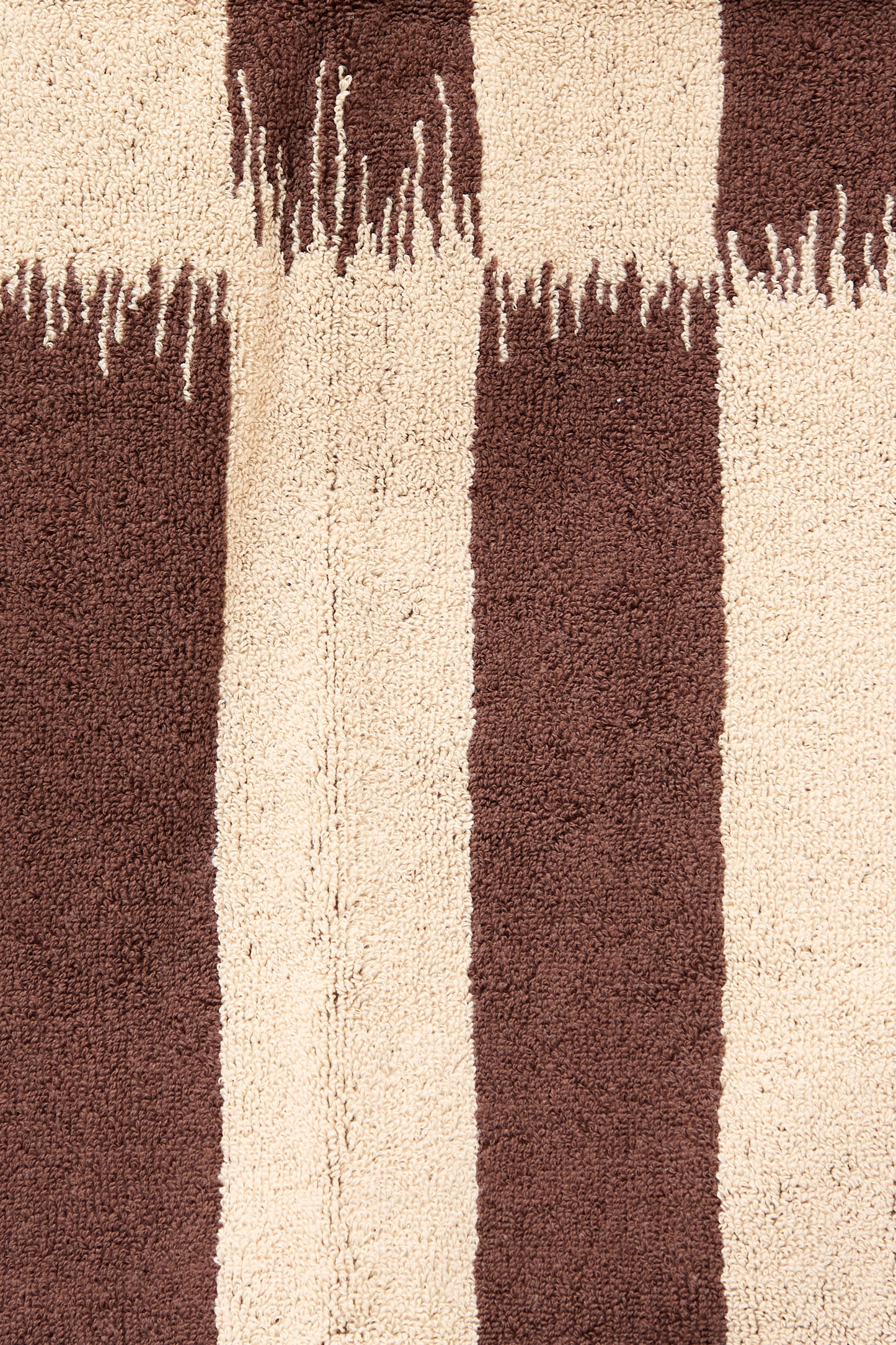 Close-up of an Autumn Sonata Karin Bath Towel featuring an Ikat weaving technique with alternating beige and brown vertical stripes, showing detailed texture and fringe edges.