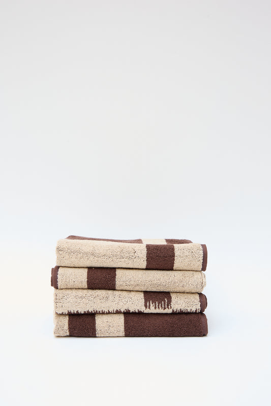 A stack of three folded Karin Hand Towels in alternating brown and beige stripes, made with organic cotton, set against a plain white background by Autumn Sonata.