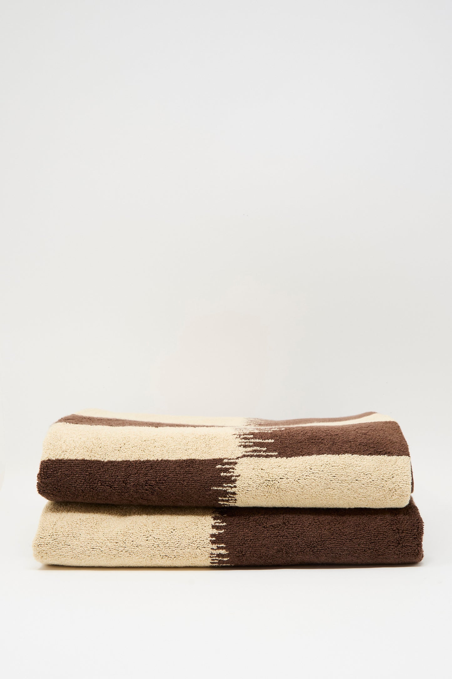 Two Karin Bath Towels by Autumn Sonata, featuring horizontal beige and brown color blocks, crafted from organic cotton and stacked on a plain white background.