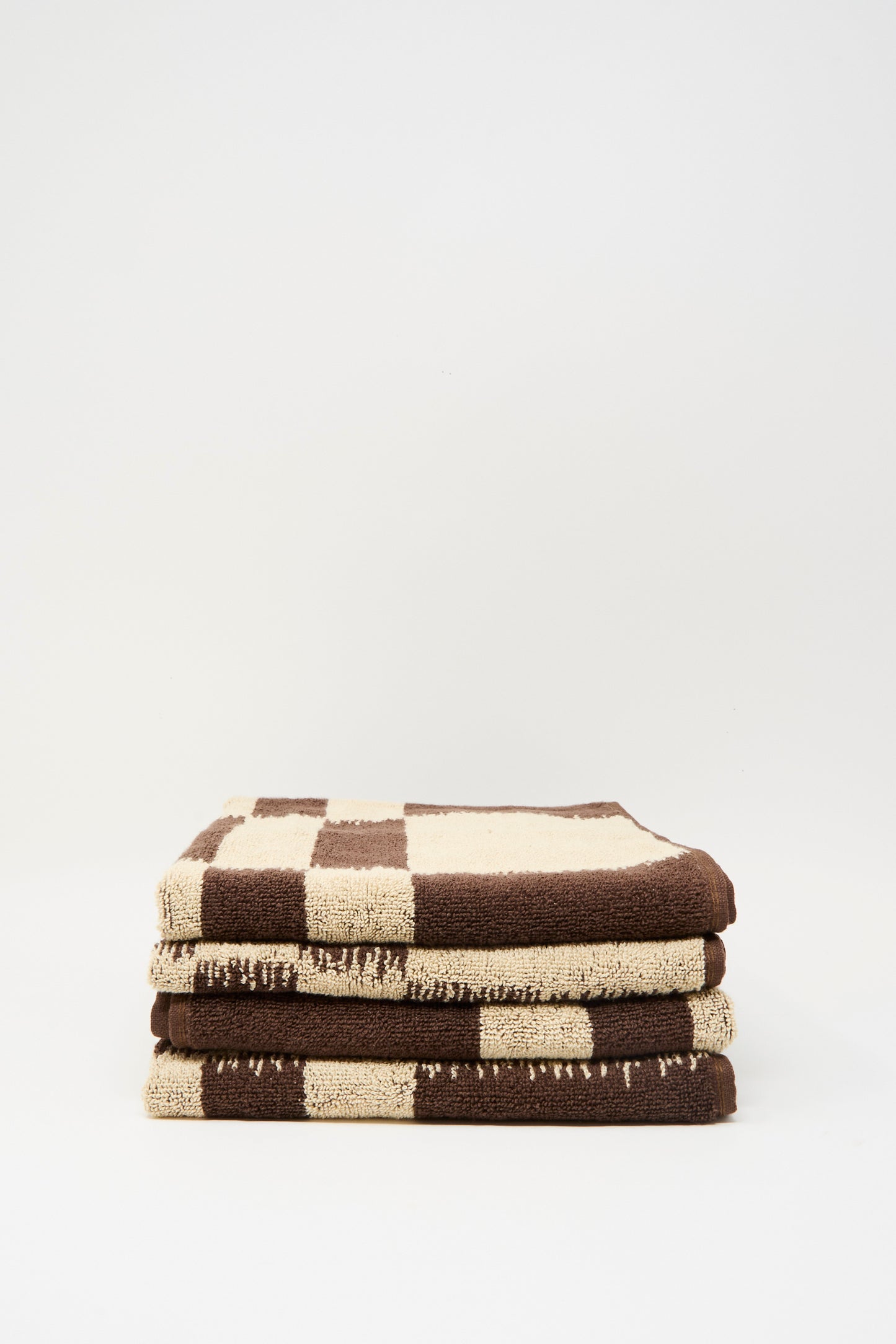 A stack of three Autumn Sonata Karin Hand Towels with a brown and beige checkerboard pattern, made from organic cotton, displayed against a plain white background.